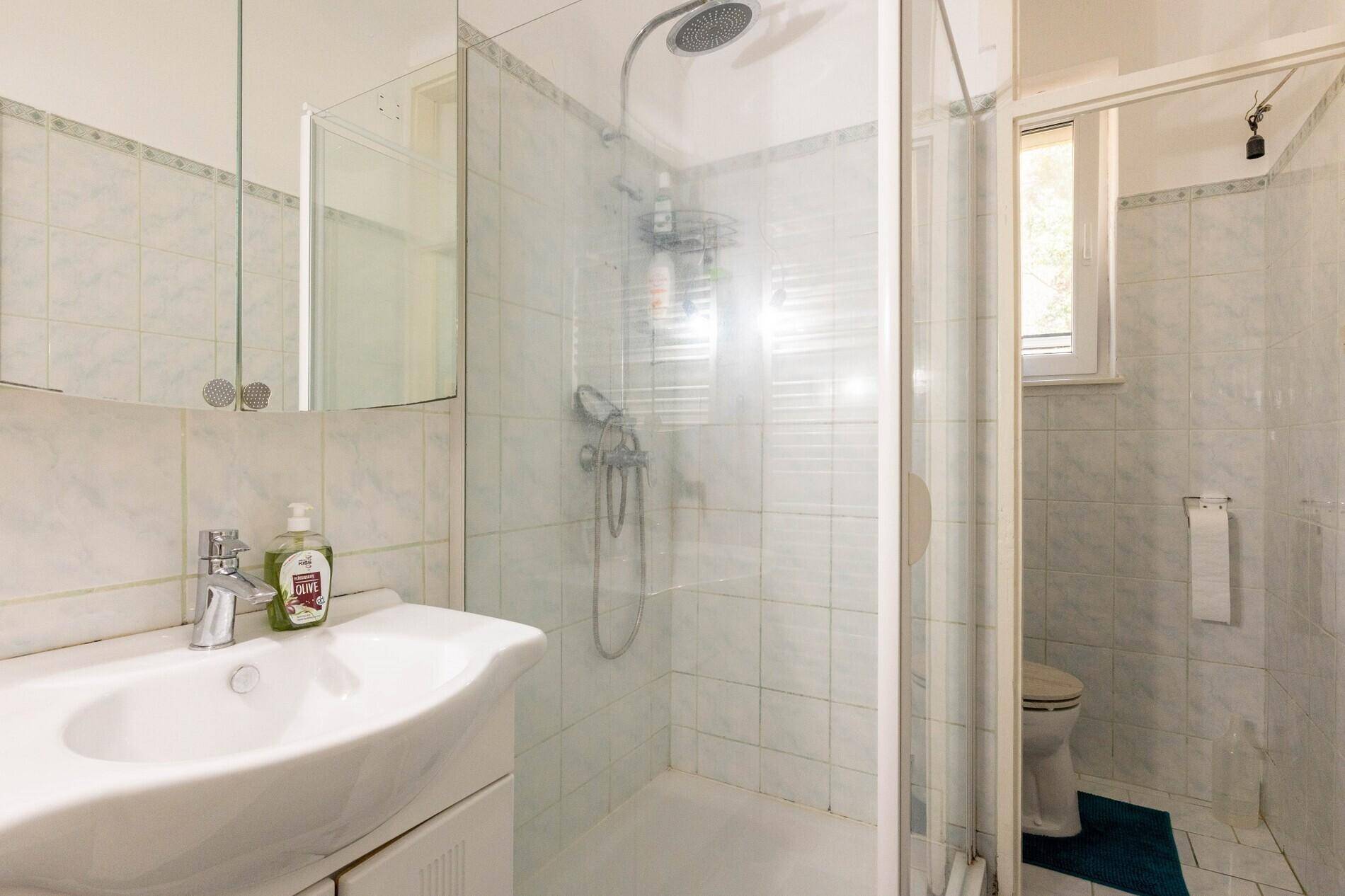 Helles Badezimmer mit Dusche, Waschbecken und Fenster für natürliche Belüftung.