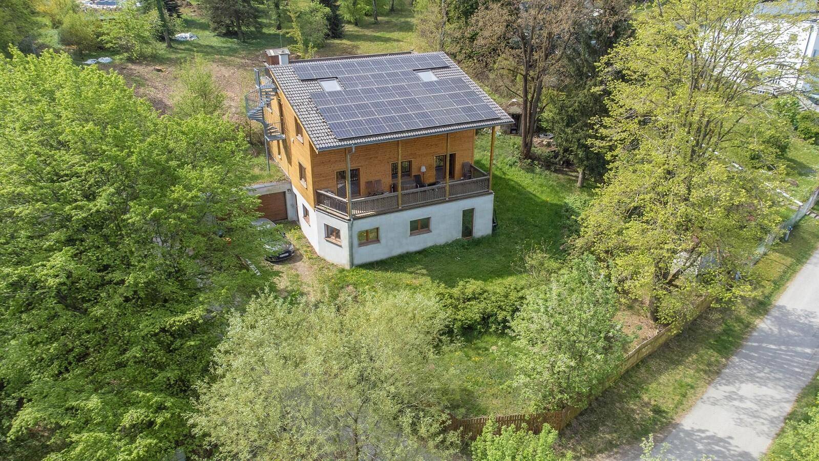 Vogelperspektive des Holzhauses mit Solaranlage und umliegender bewaldeter Landschaft.