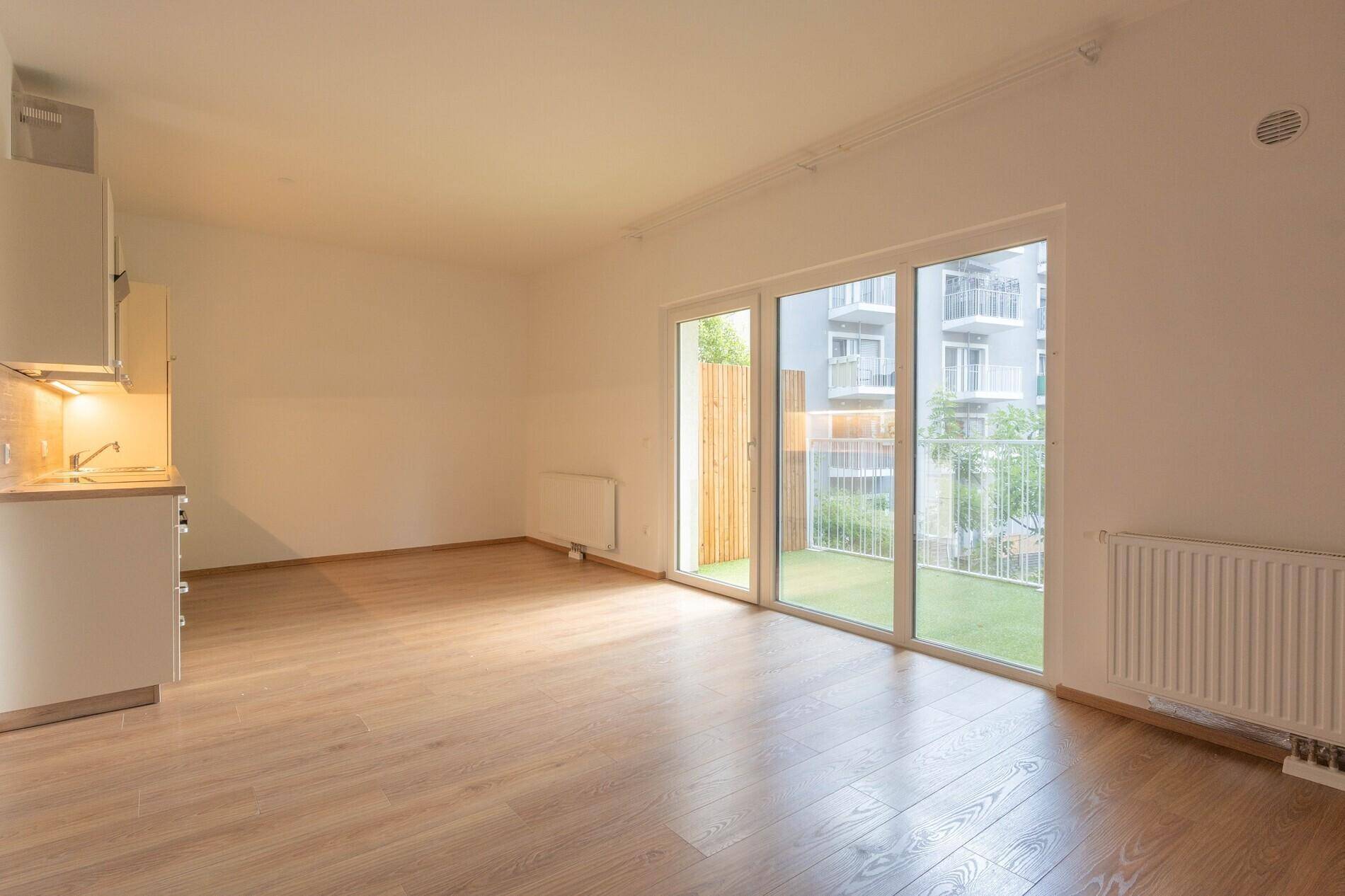 Heller Wohnbereich mit Holzboden und großen Fenstern, die Zugang zu einem kleinen Außenbereich bieten.