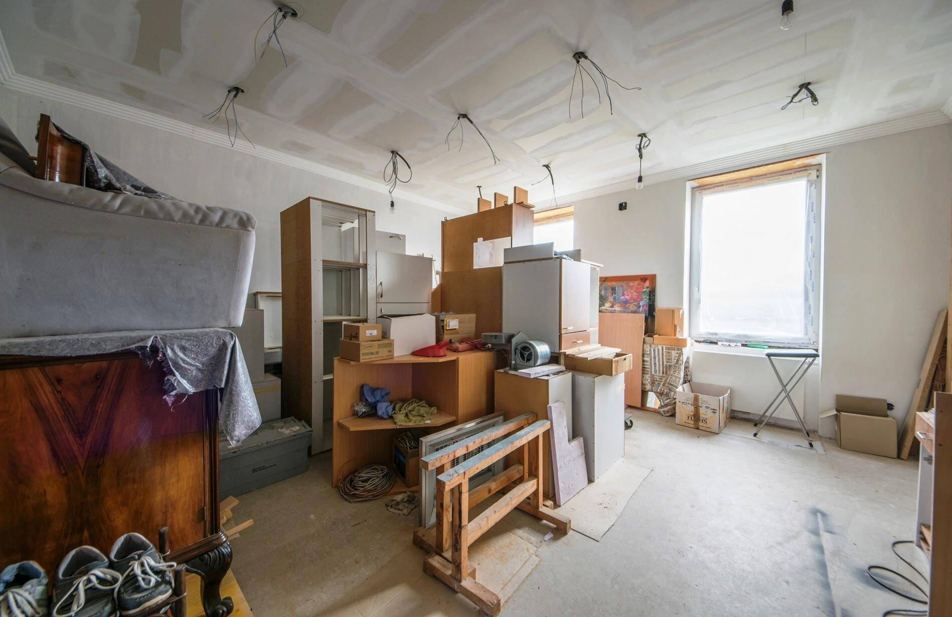 Raum in Renovierung mit vielen Kartons, Baumaterialien und provisorischer Beleuchtung.