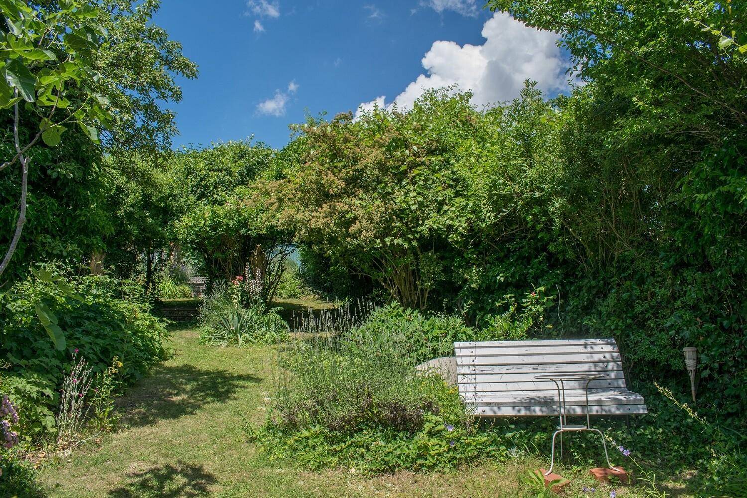 Idyllischer Garten mit üppiger Vegetation, Rasenflächen und einer Holzbank zum Entspannen.