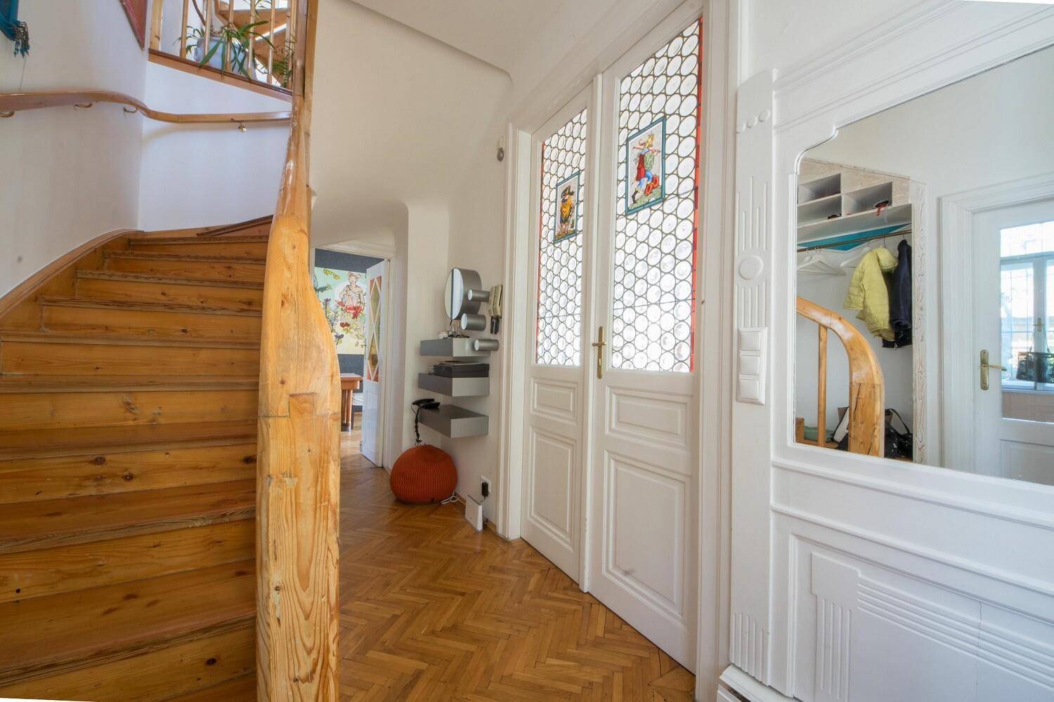 Heller Flur mit geschwungener Holztreppe, Parkettboden und dekorativen Glastüren.