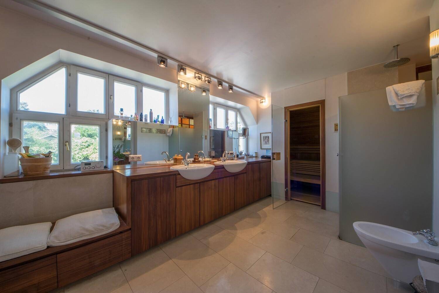 Geräumiges Badezimmer mit Doppelwaschbecken, großer Fensterfront und integrierter Sauna für Wellness.