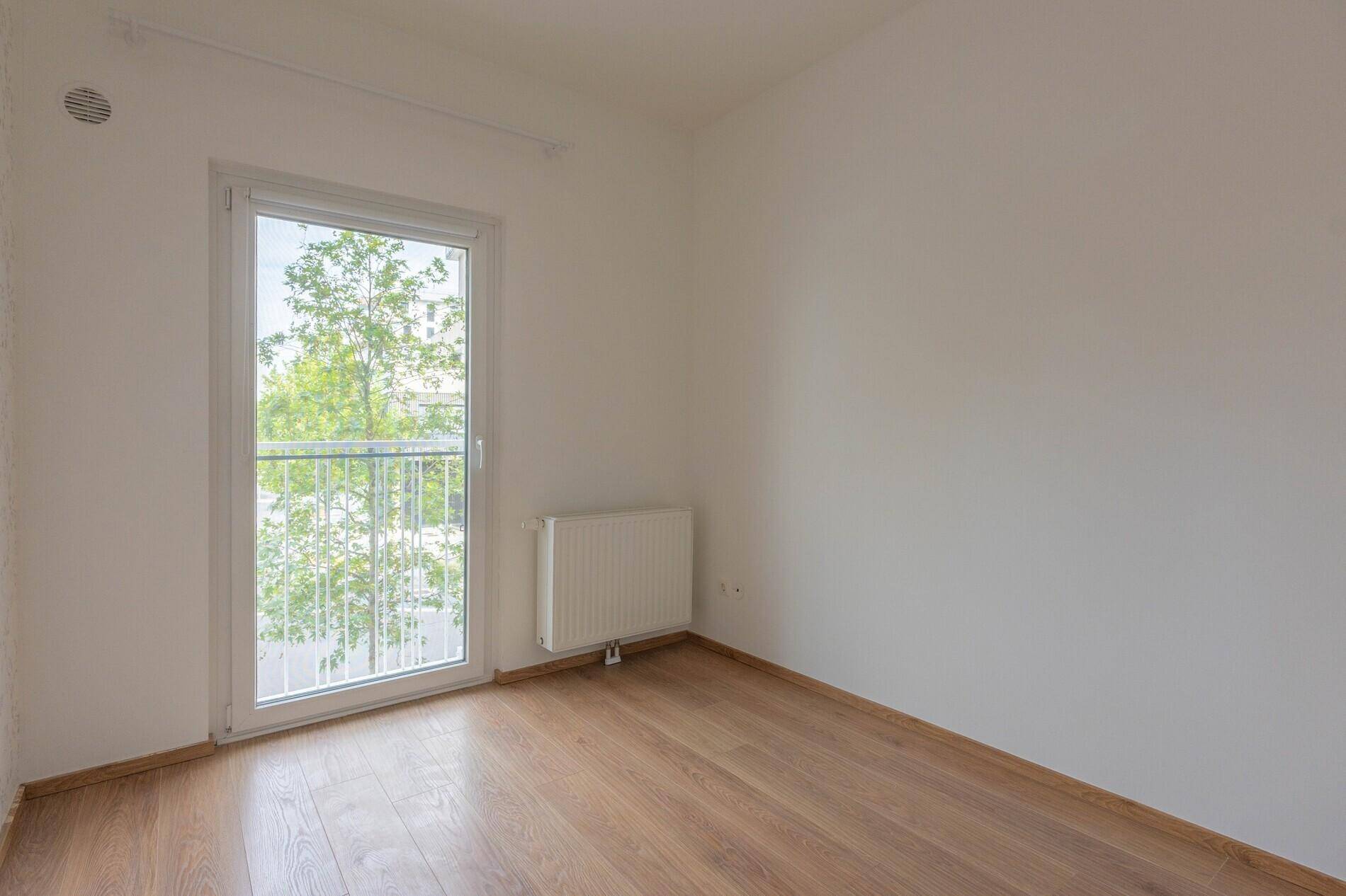 Leeres Schlafzimmer mit Holzboden und Zugang zu einem kleinen Balkon oder einer französischen Balkontür.