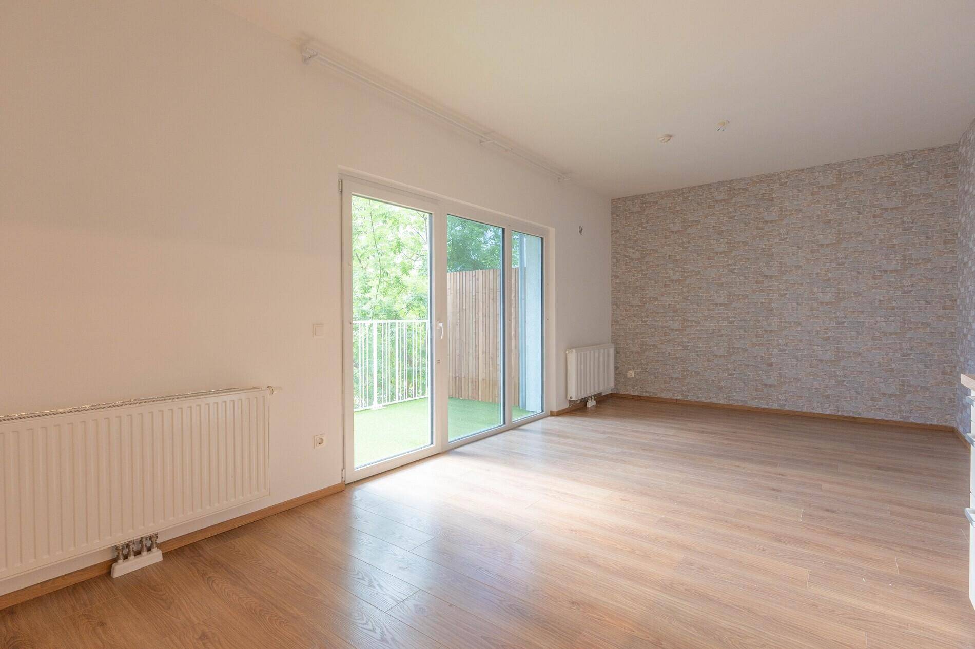 Geräumiger Raum mit Holzboden, einer Akzentwand und Zugang zu einem Balkon durch große Schiebetüren.