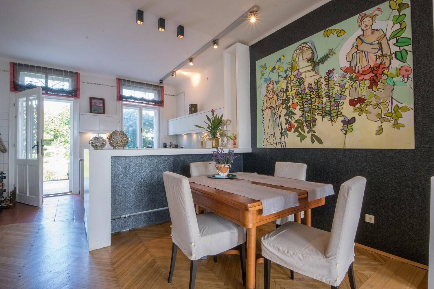 Essbereich mit Holztisch und Stühlen, angrenzend an eine halb-offene Küche mit moderner Kunst an der Wand.