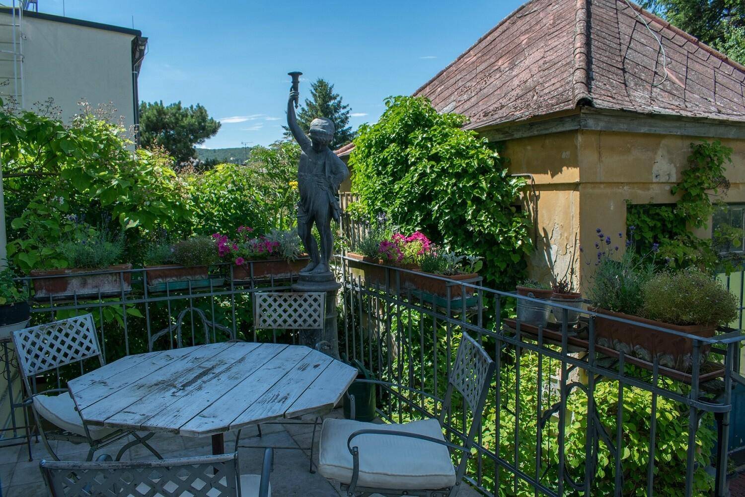 Malerische Terrasse mit schmiedeeisernem Geländer, Gartenmöbeln und einer antiken Statue.