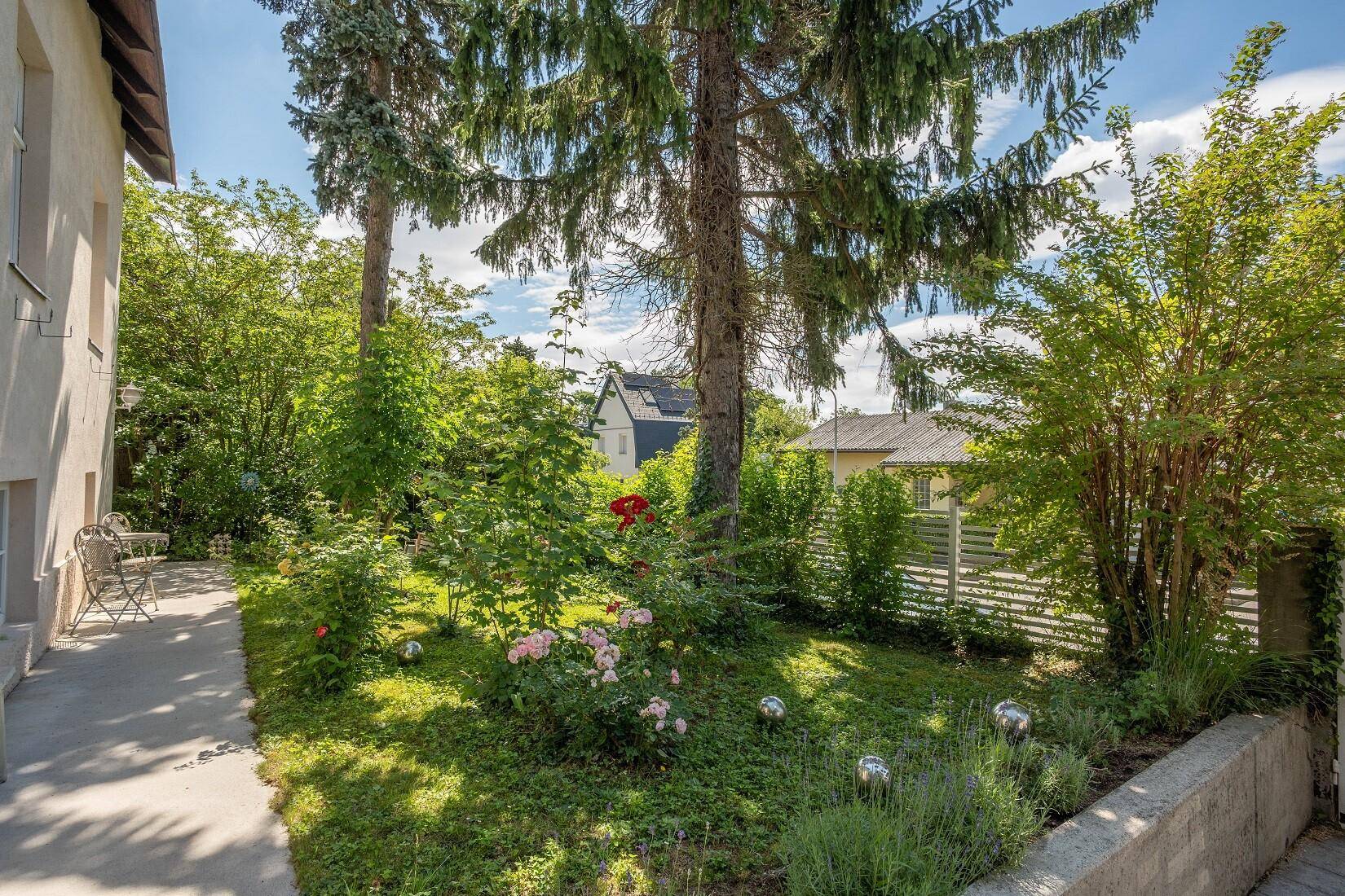 Seitlicher Gartenbereich mit Blumenbeeten, Sträuchern und einem kleinen Weg.