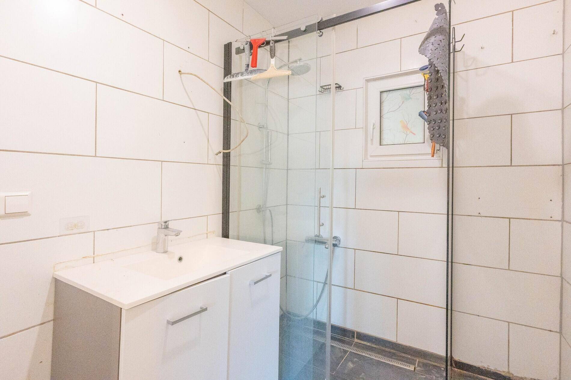 Modernes Badezimmer mit weißen Fliesen, Duschkabine und Einzelwaschbecken.