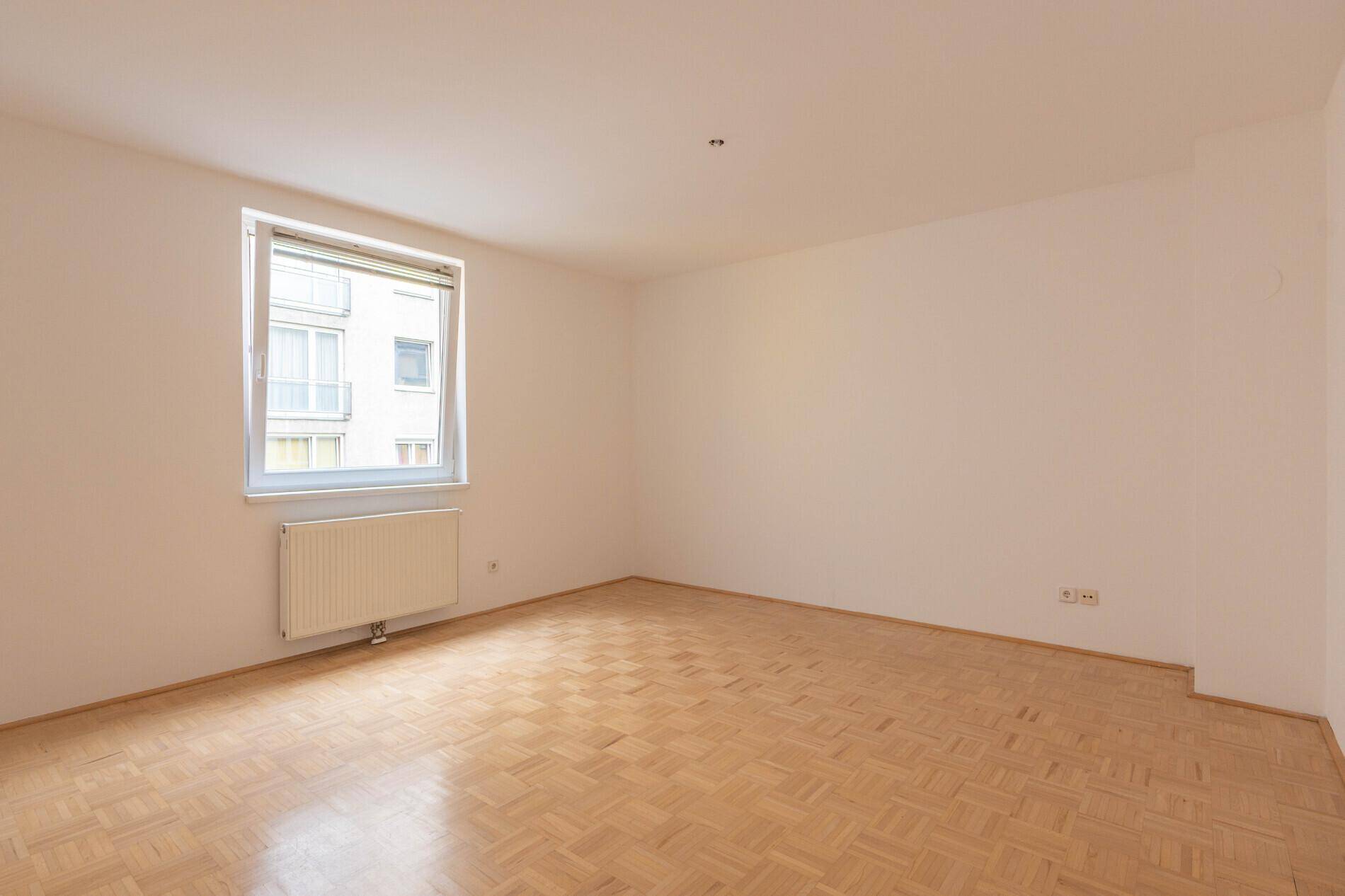 Ruhiges Schlafzimmer mit Parkettboden und einem großen Fenster, das eine angenehme Atmosphäre schafft.