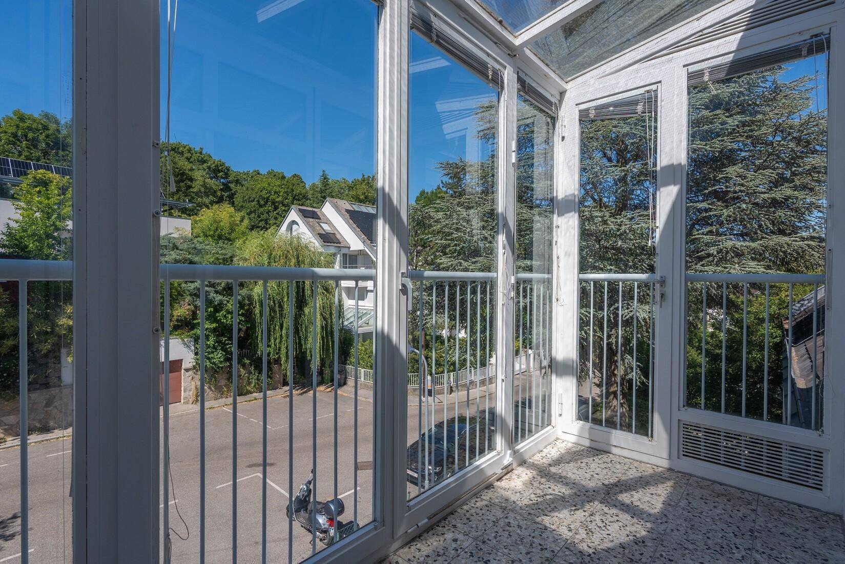 Verglaster Balkon mit weitem Blick auf die umliegende Wohngegend und viel Grün.