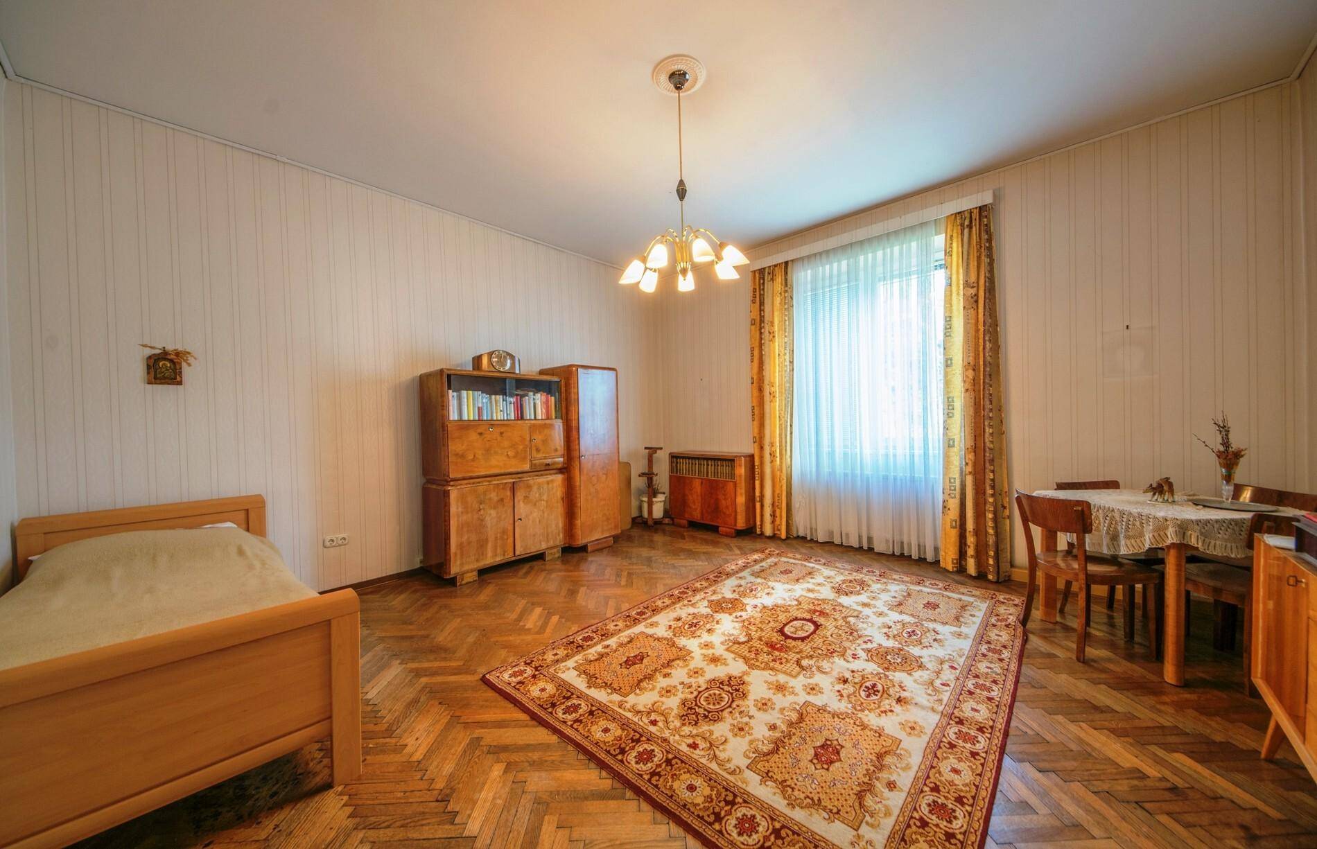 Helles Zimmer mit Fischgrätparkett, einem Einzelbett und traditionellen Holzmöbeln.