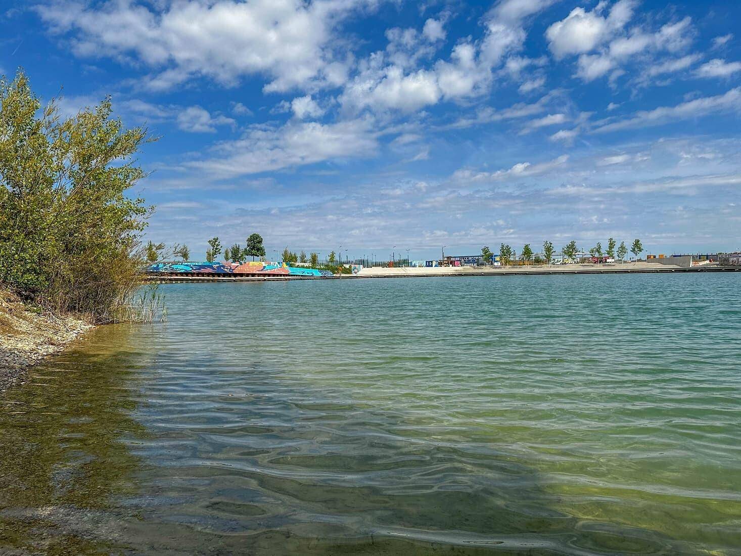 Weitläufiger Blick auf einen See oder Teich unter blauem Himmel mit leichter Bewölkung.