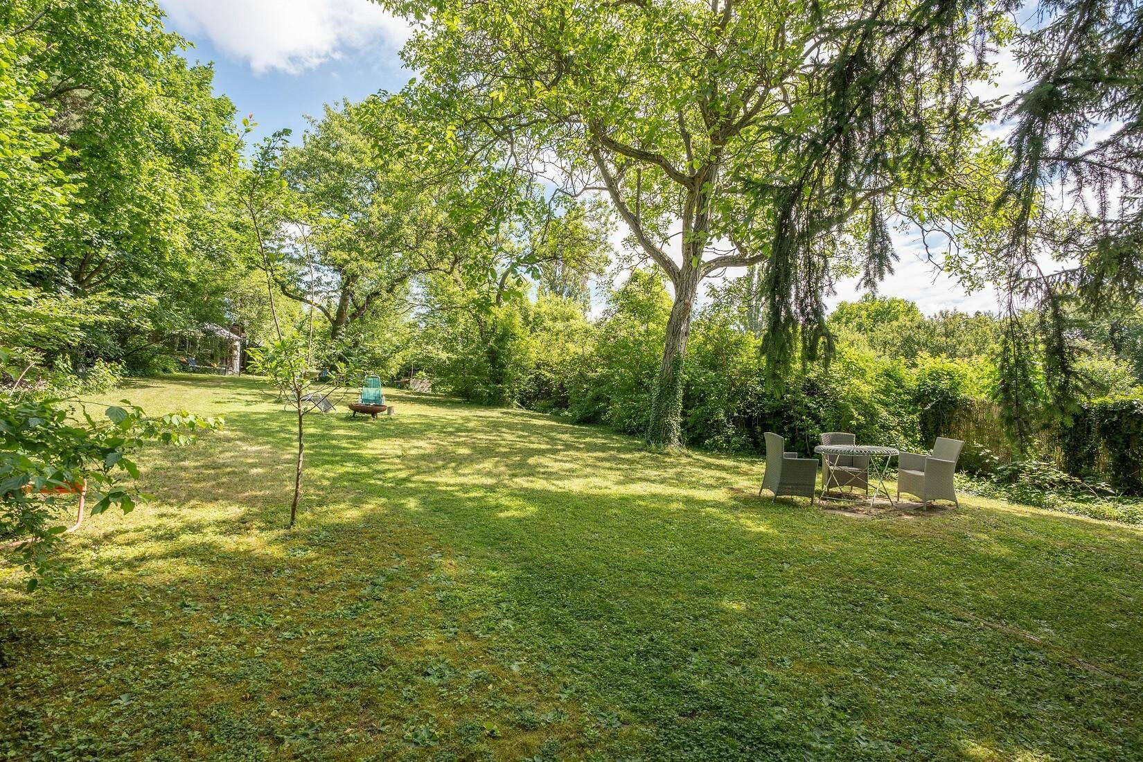 Gepflegter Garten mit Rasenfläche, altem Baumbestand und einem Essbereich im Freien.