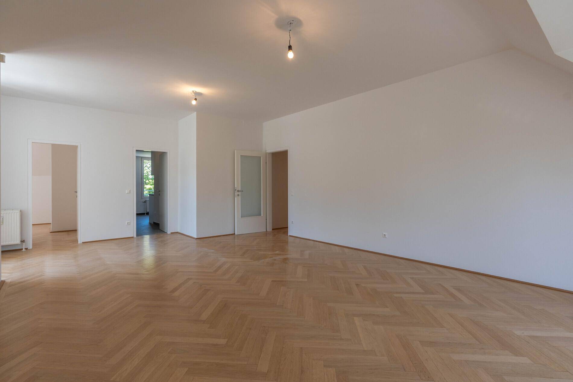 Heller Wohnraum mit elegantem Fischgrätparkett und mehreren Türen zu angrenzenden Zimmern.