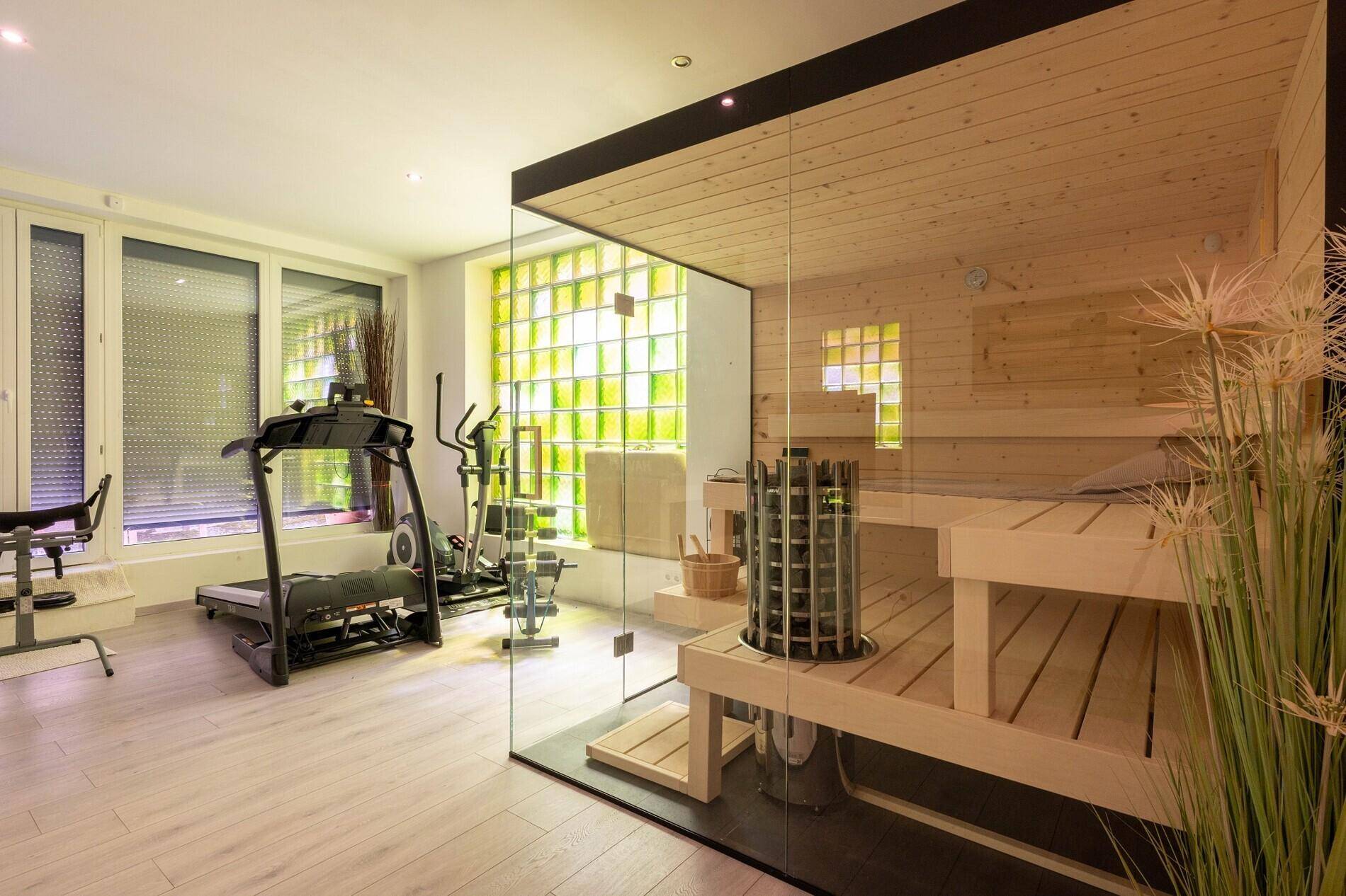 Fitnessraum mit integrierter Sauna, Trainingsgeräten und großen Fenstern.