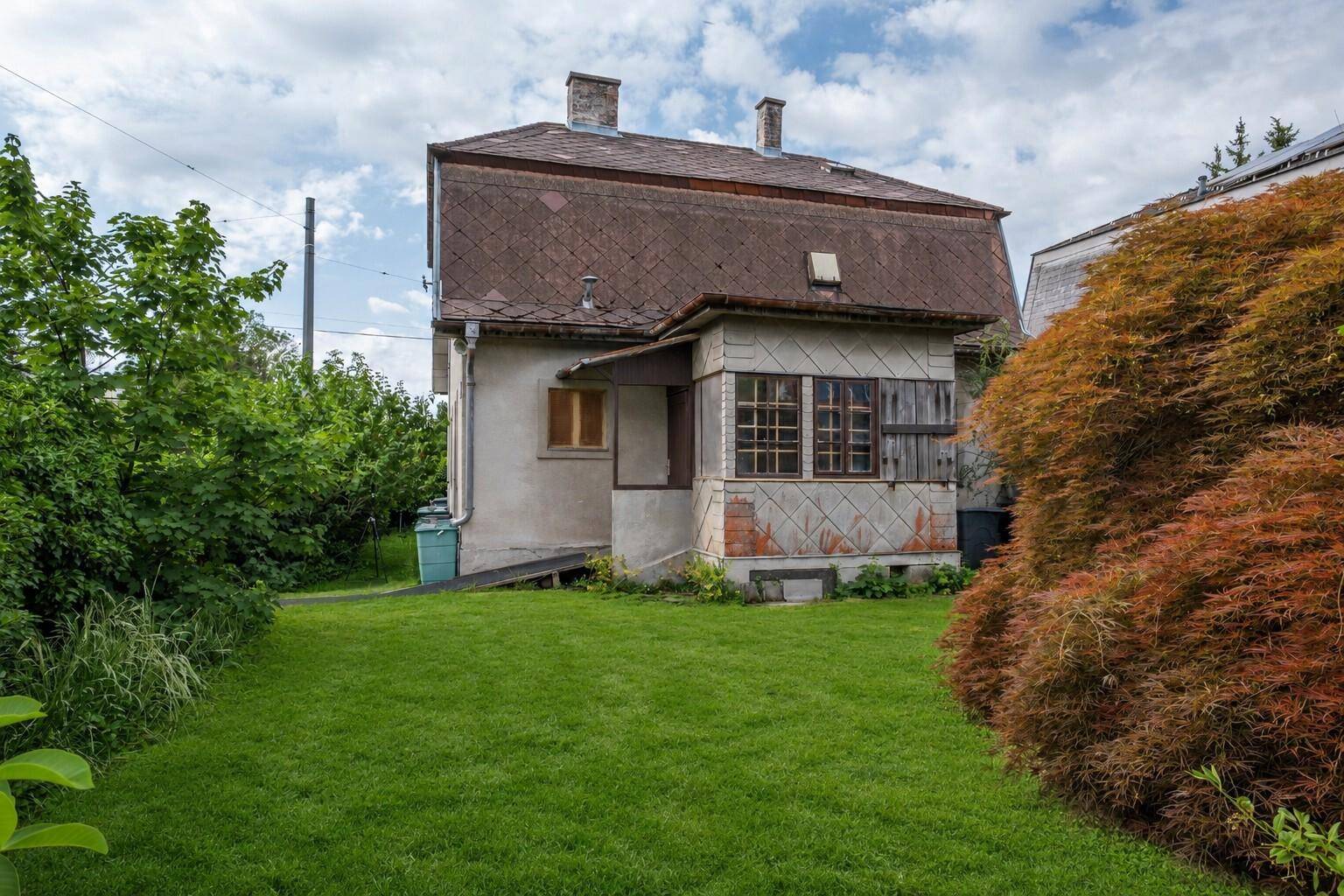 Rückansicht des Hauses vom grünen Garten aus, mit einem markanten roten Baum im Vordergrund.
