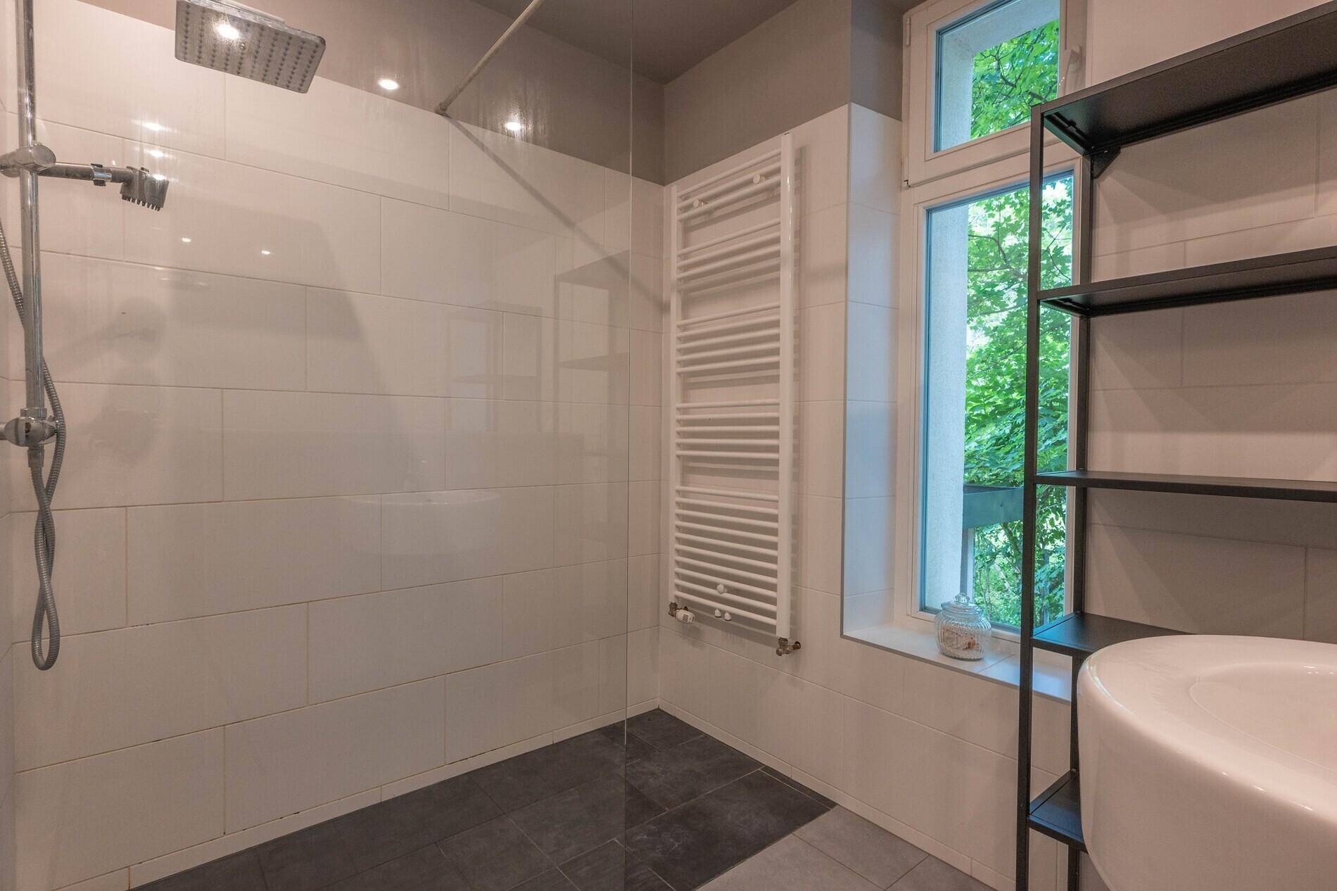 Modernes Badezimmer mit großer begehbarer Dusche, Fenster und Handtuchheizkörper.
