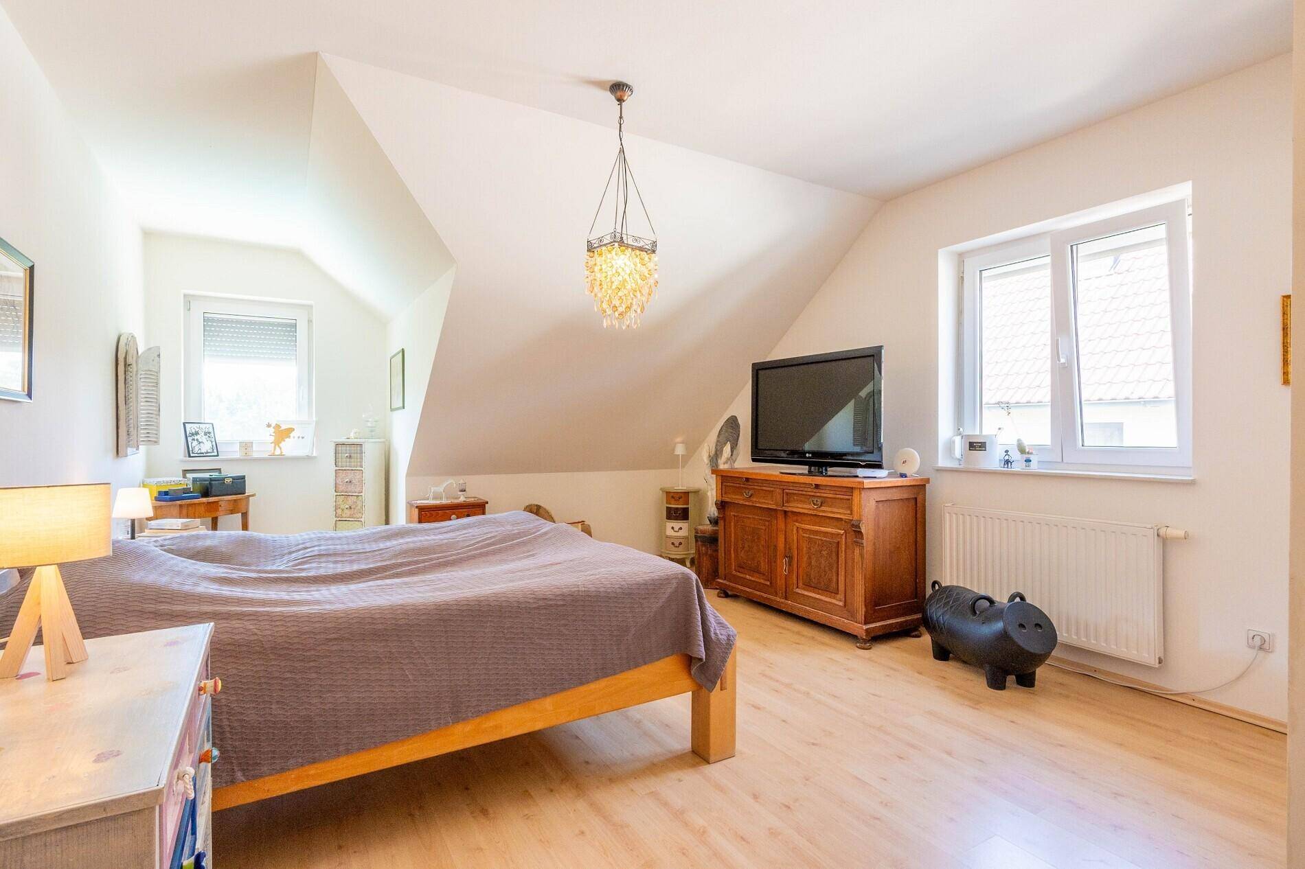 Geräumiges Schlafzimmer im Dachgeschoss mit Holzboden, schrägen Wänden und Fenster.