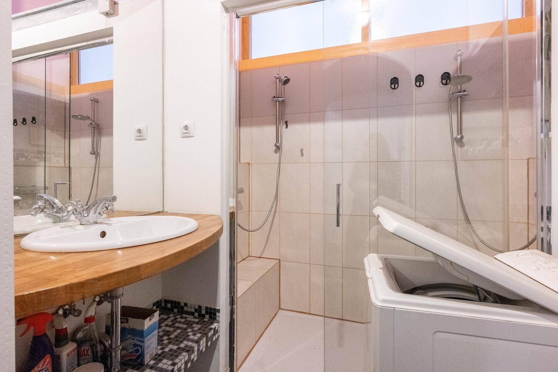 Badezimmer mit Waschbecken, Holzarbeitsplatte und einer geräumigen Duschkabine.