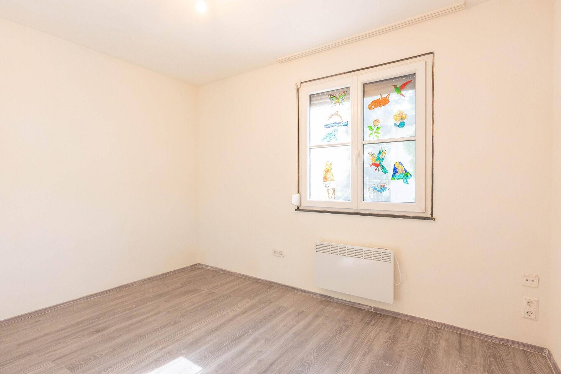 Kinderzimmer mit hellem Laminatboden und Fenster mit bunten Dekorationen.