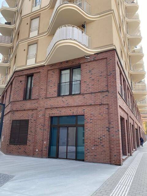 Ecke eines modernen Gebäudes mit Ziegelfassade im Erdgeschoss und geschwungenen Balkonen in den oberen Etagen.