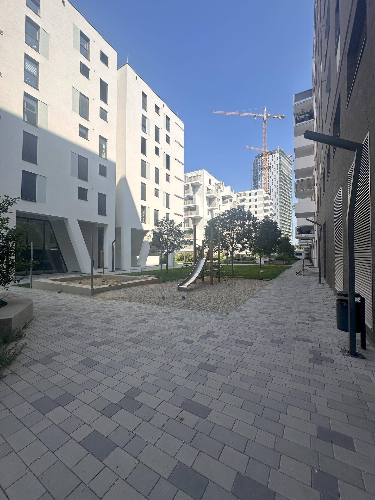 Moderner Innenhof mit einem Sandkasten und einer Rutsche, umgeben von Wohngebäuden, ideal für Kinder.