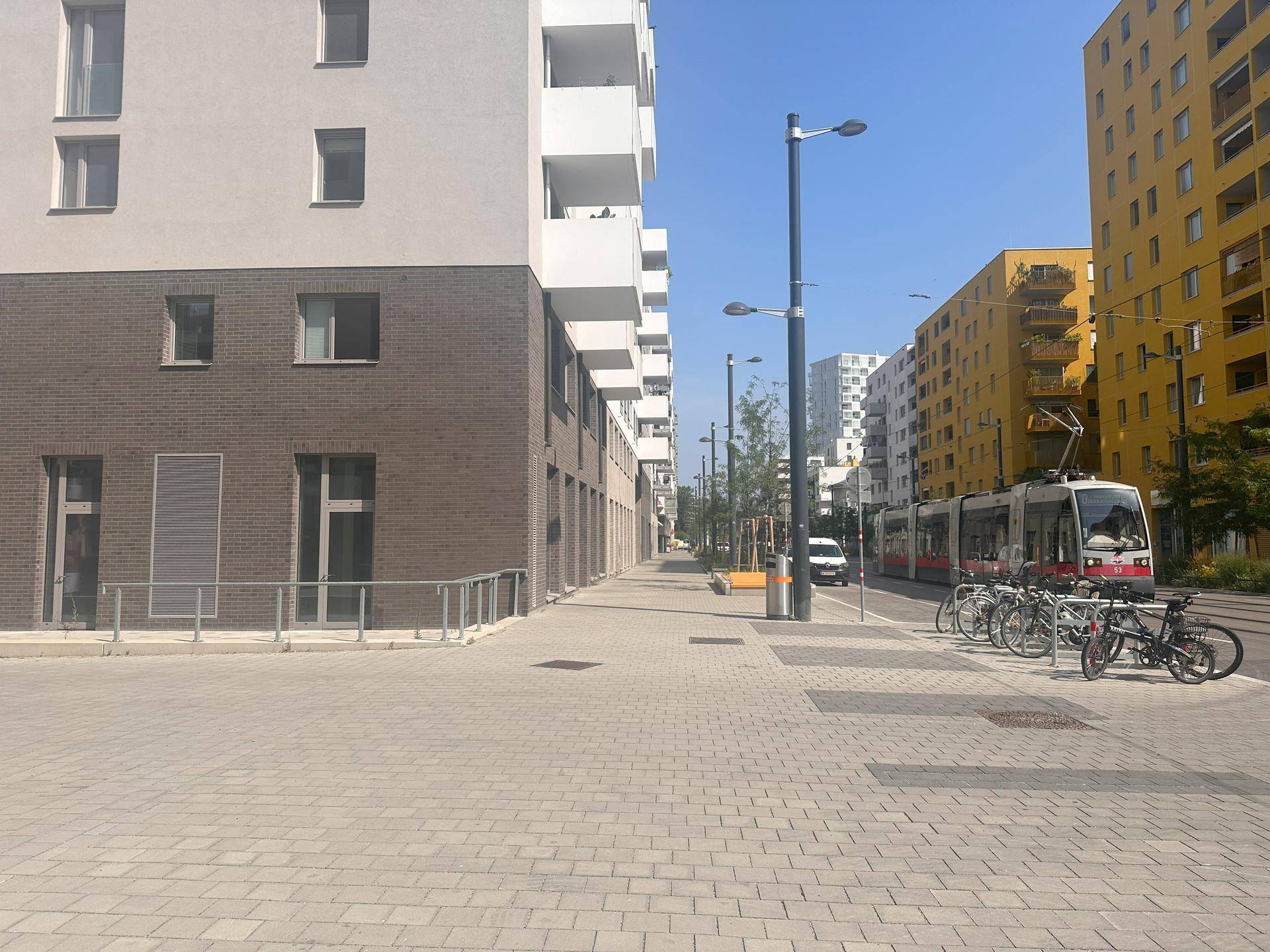 Städtische Straße mit modernen Gebäuden, Straßenbahnschienen und geparkten Fahrrädern unter klarem blauem Himmel.