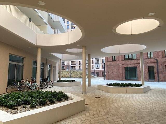 Moderner Innenhof mit runden Deckenöffnungen, begrünten Beeten und Fahrradabstellplätzen.