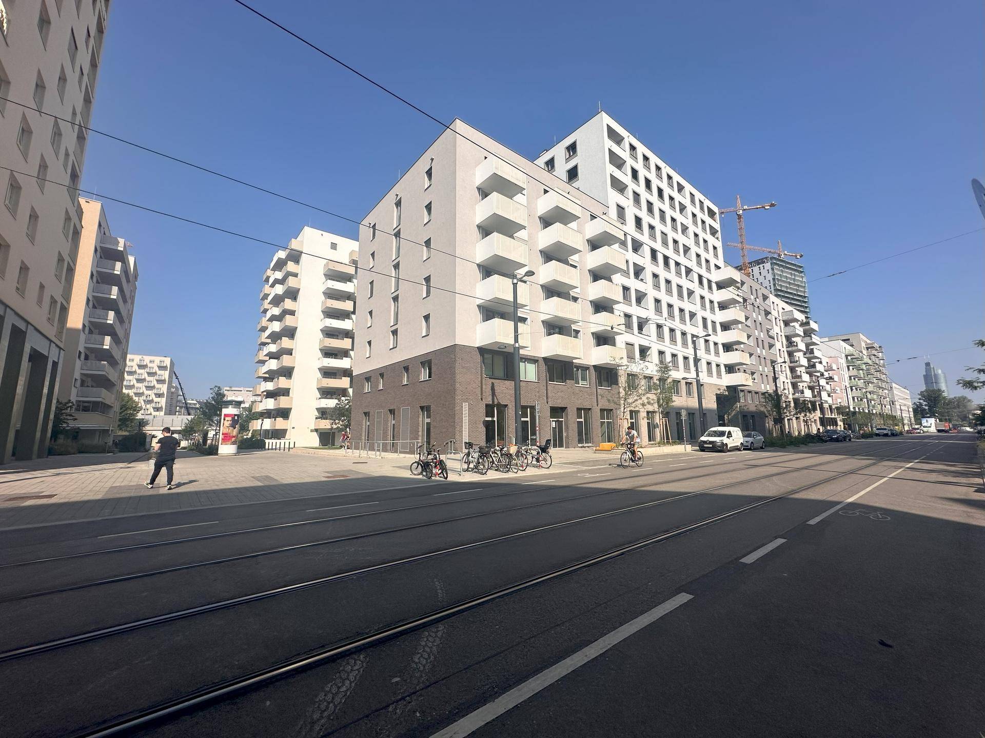 Breite Straße mit modernen Wohngebäuden, Straßenbahnschienen und gepflasterten Gehwegen unter klarem Himmel.