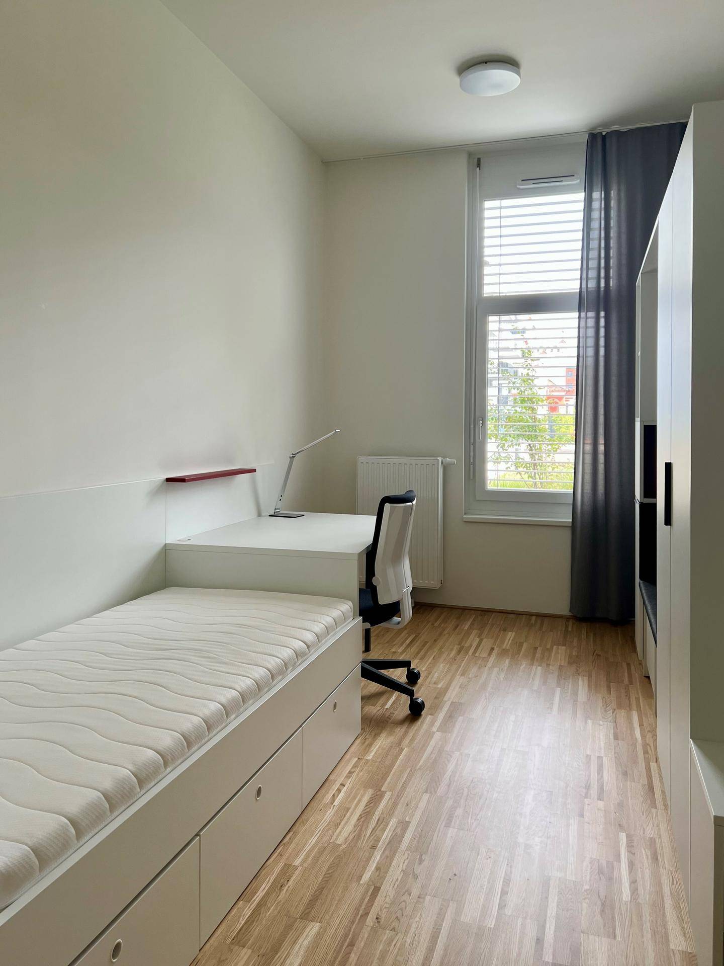Modernes Schlafzimmer mit Schreibtisch, Bett und großem Fenster für viel Tageslicht.