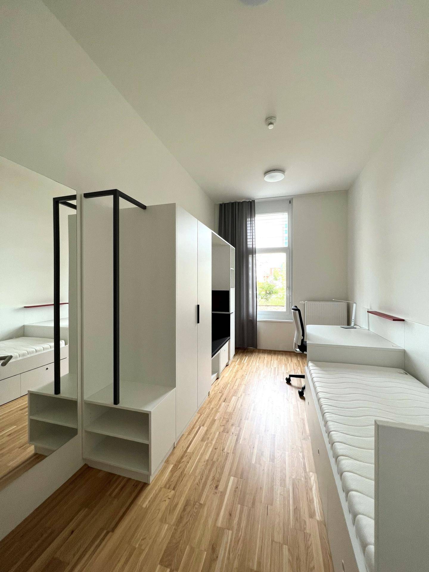 Helles Schlafzimmer mit Einzelbett, Schreibtisch und integrierten Schränken, ideal für Studenten.