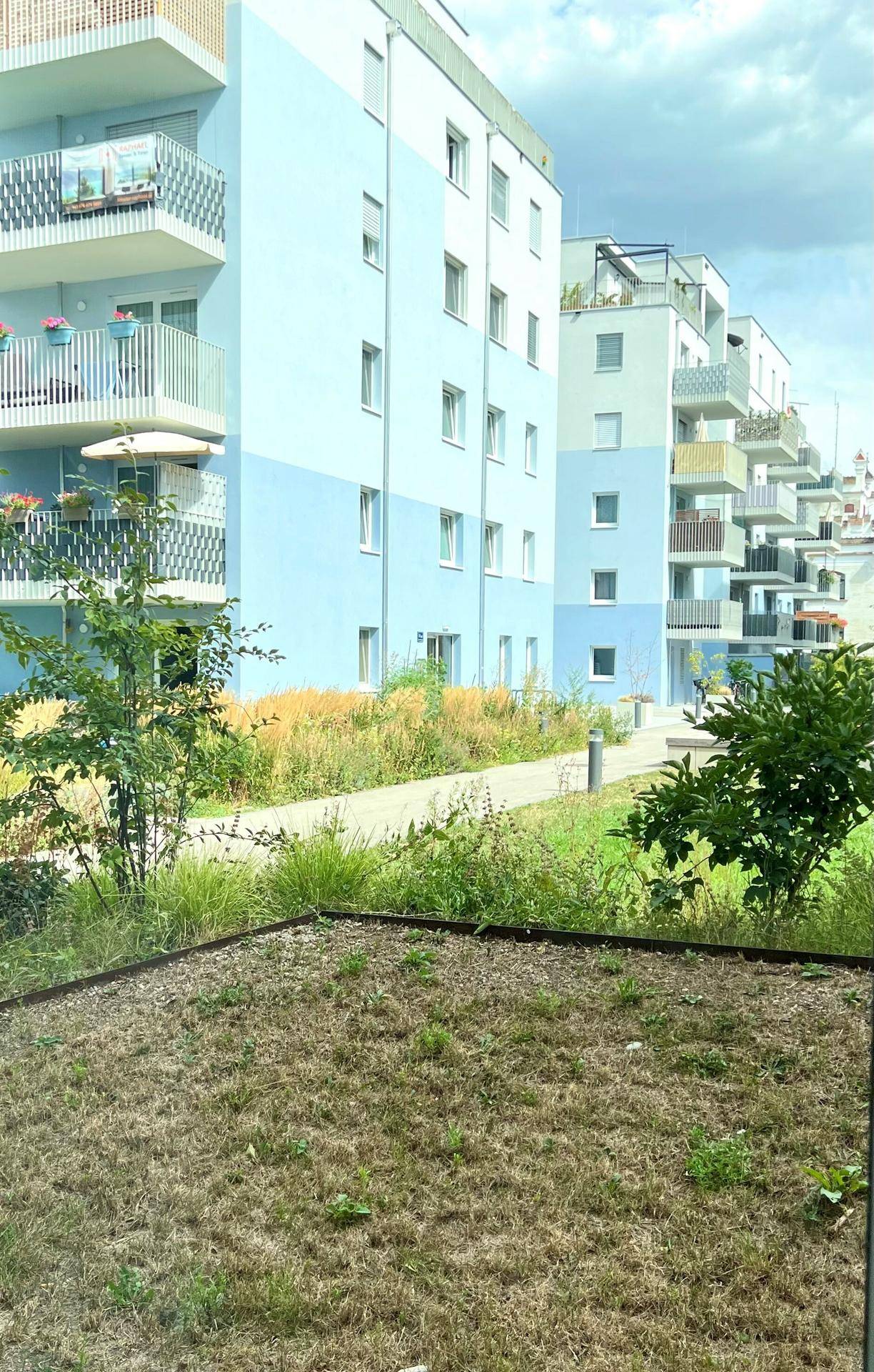 Mehrere moderne Wohngebäude mit blauer Fassade und Balkonen in einer grünen Umgebung.