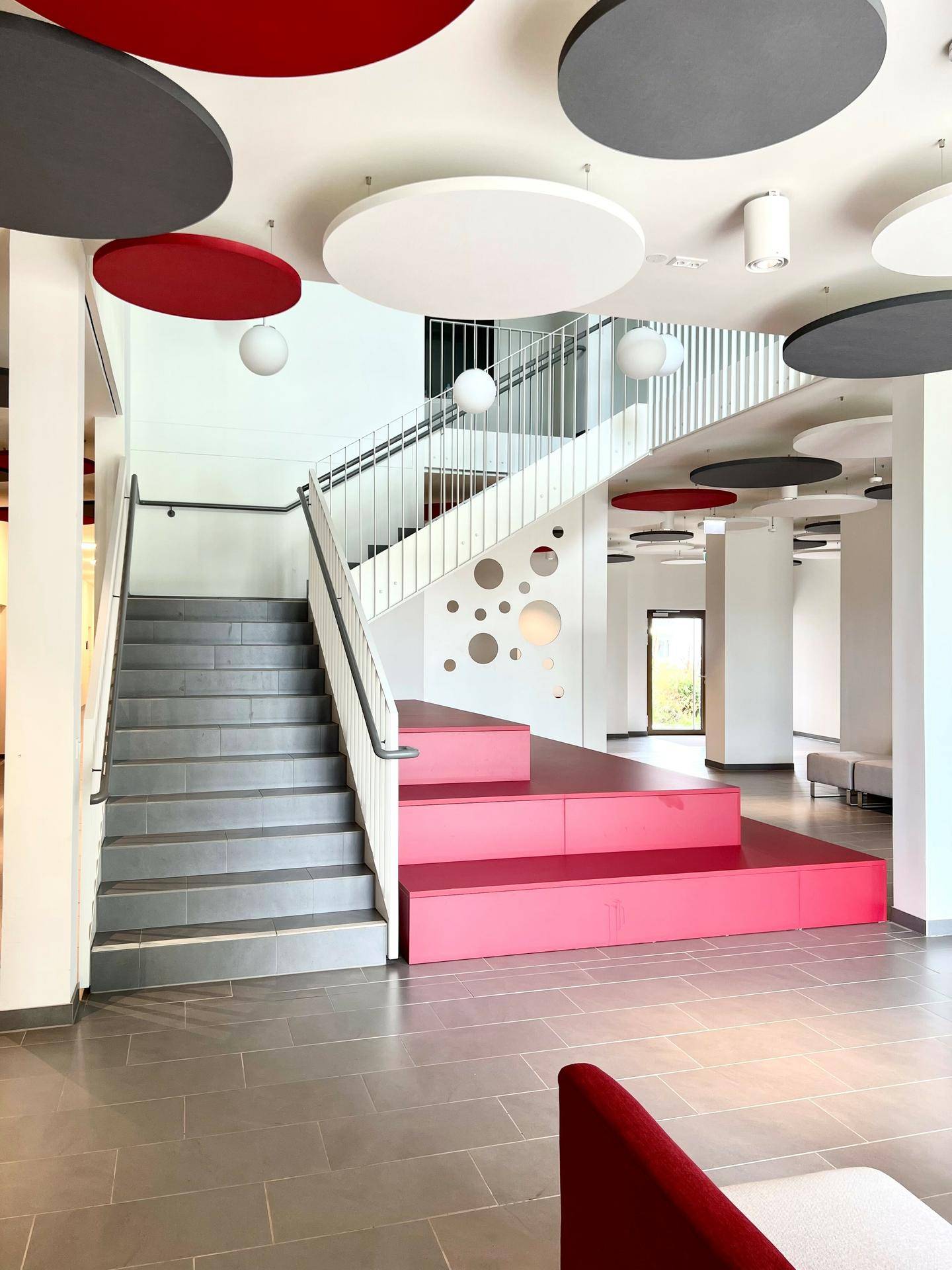 Modernes Treppenhaus mit farbigen Stufen und dekorativen Deckenelementen in einem Gemeinschaftsbereich.