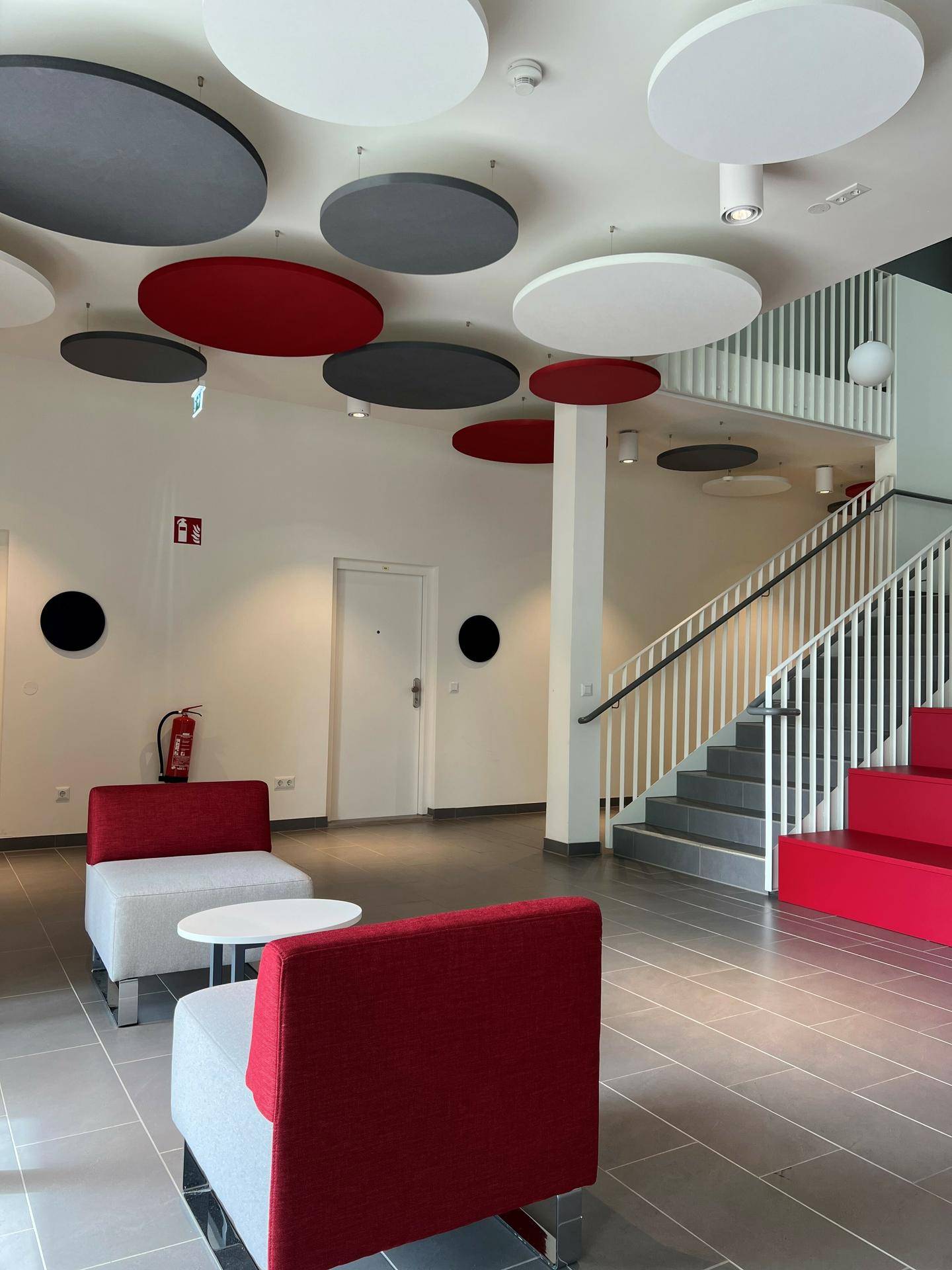 Moderner Gemeinschaftsbereich mit farbigen Deckenelementen, Sitzgelegenheiten und Treppenhaus.