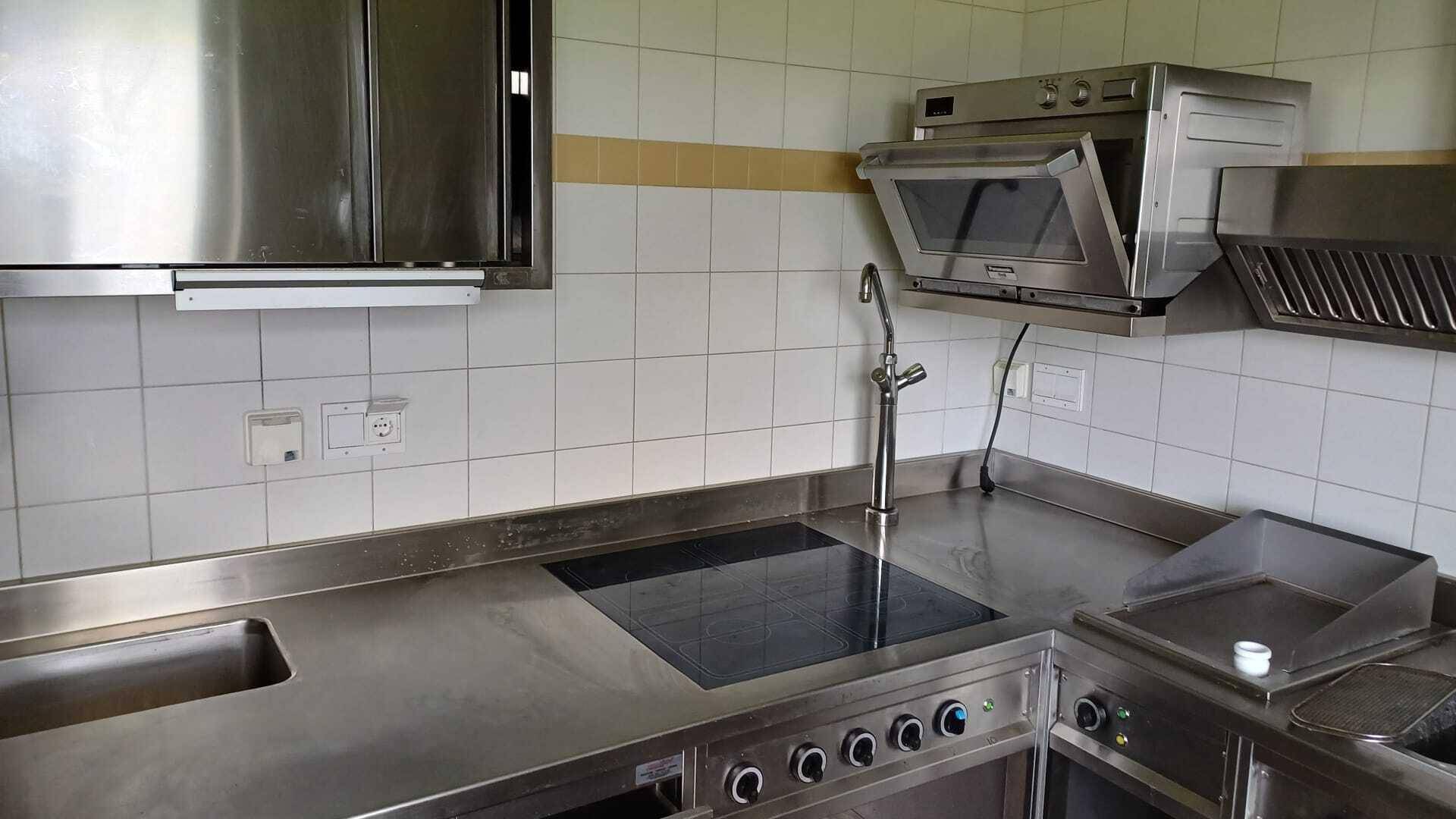 Professionelle Edelstahlküche mit Induktionskochfeld, Spülbecken und weiteren Kochgeräten.