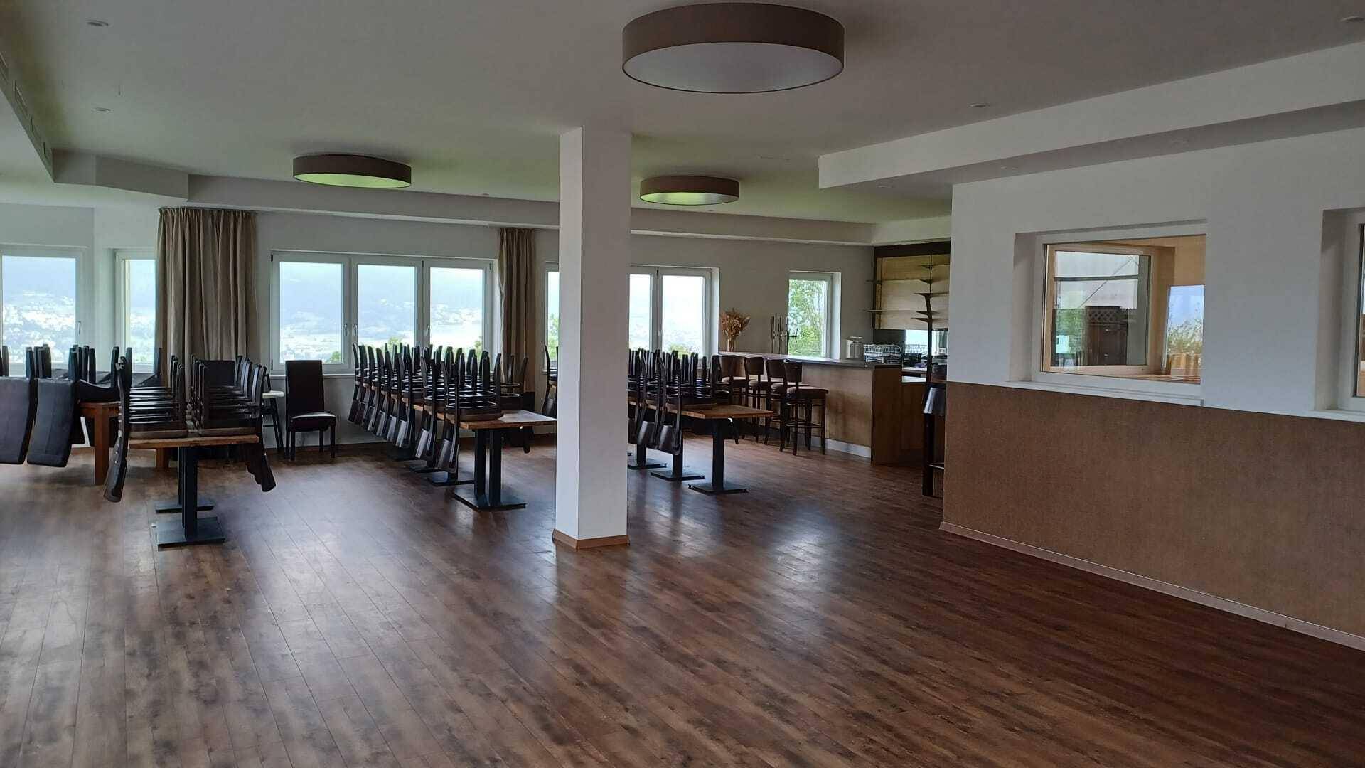 Großer, heller Speisesaal mit Holzboden, vielen Fenstern und gestapelten Stühlen, bereit für Veranstaltungen.