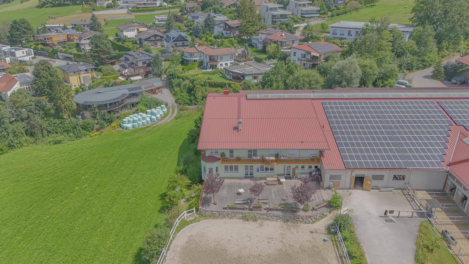 Luftaufnahme des Anwesens mit Wohngebäude, Stallungen, Reitplatz und Photovoltaikanlage auf dem Dach.