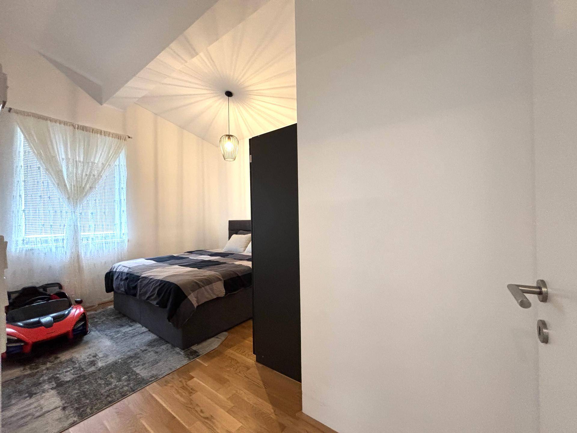 Helles Schlafzimmer mit Holzboden, Fenster und Blick auf den Außenbereich.