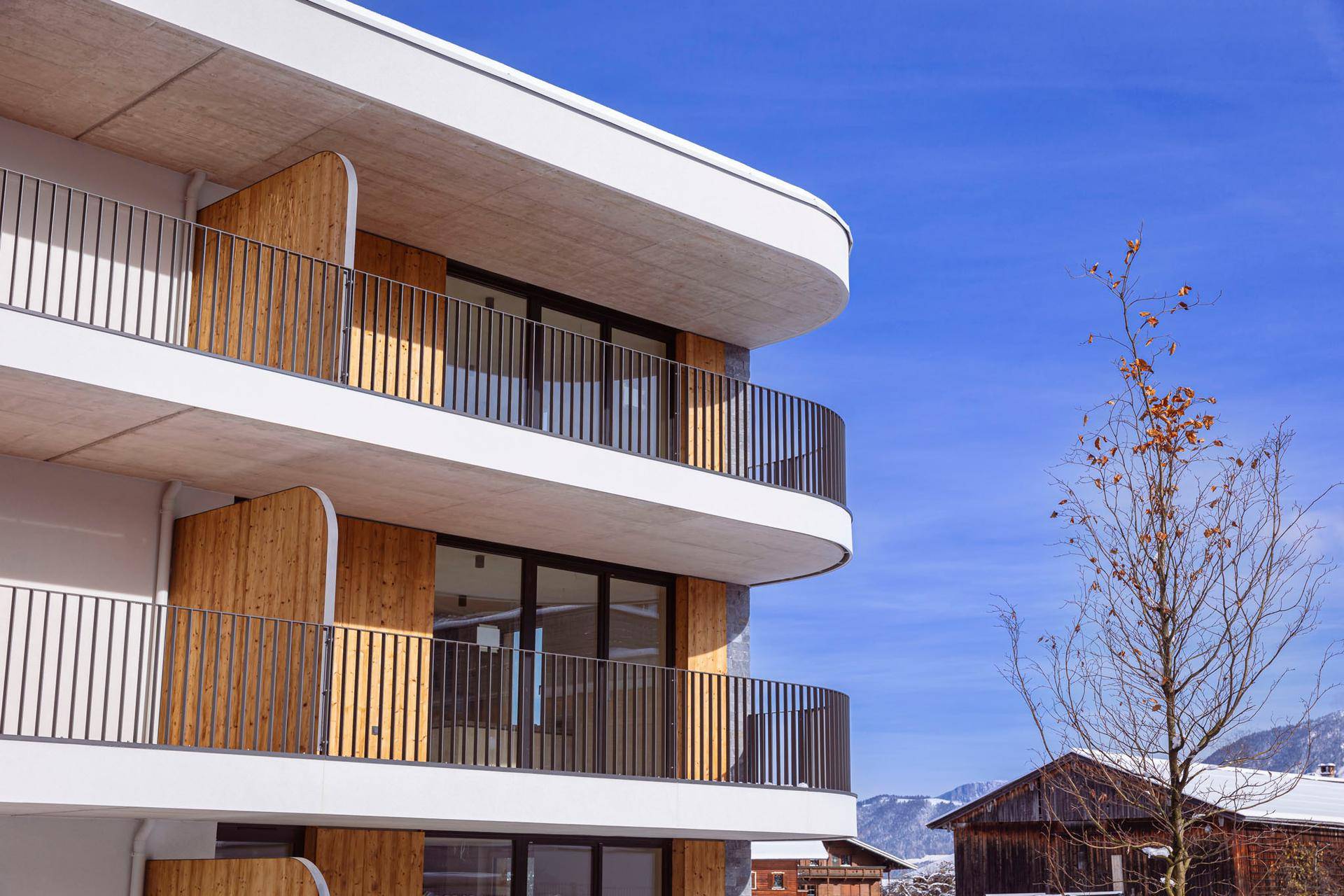 Geschwungene Balkone mit Metallgeländern und Holzverkleidung unter blauem Winterhimmel.