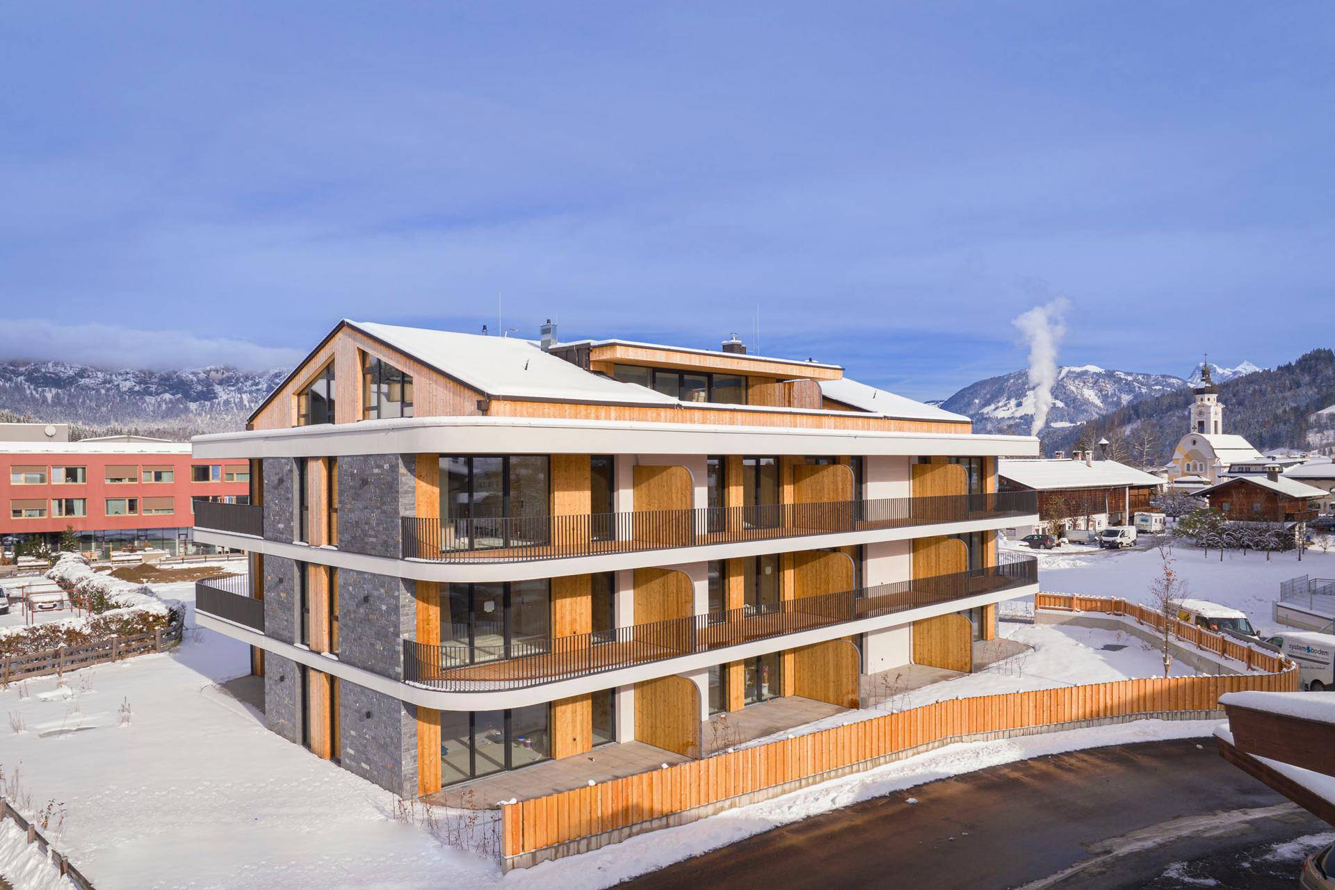 Neubau-Apartmenthaus mit moderner Architektur und Steinverkleidung in verschneiter Dorflandschaft.