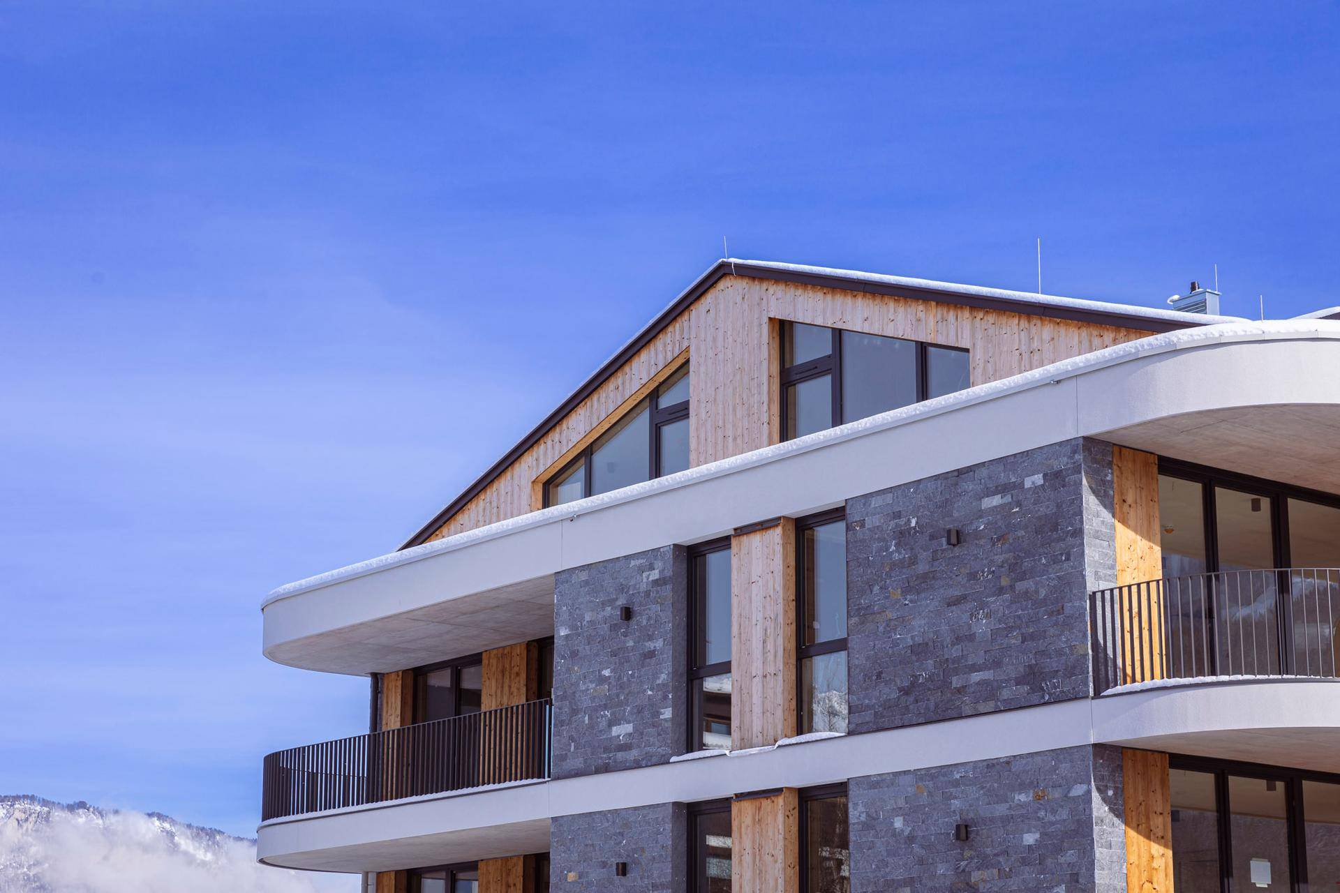 Detailansicht der modernen Fassade mit Naturstein, Holzverkleidung und eleganten Balkonen.