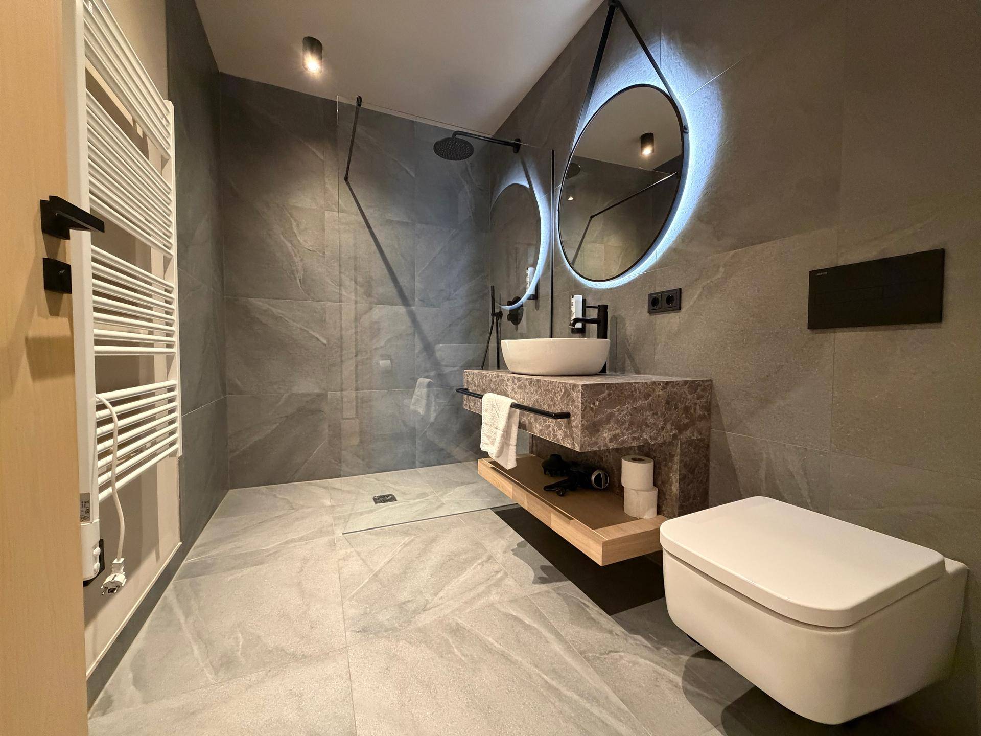 Modernes Badezimmer mit grauen Fliesen, ebenerdiger Dusche und stilvollem Waschtisch.