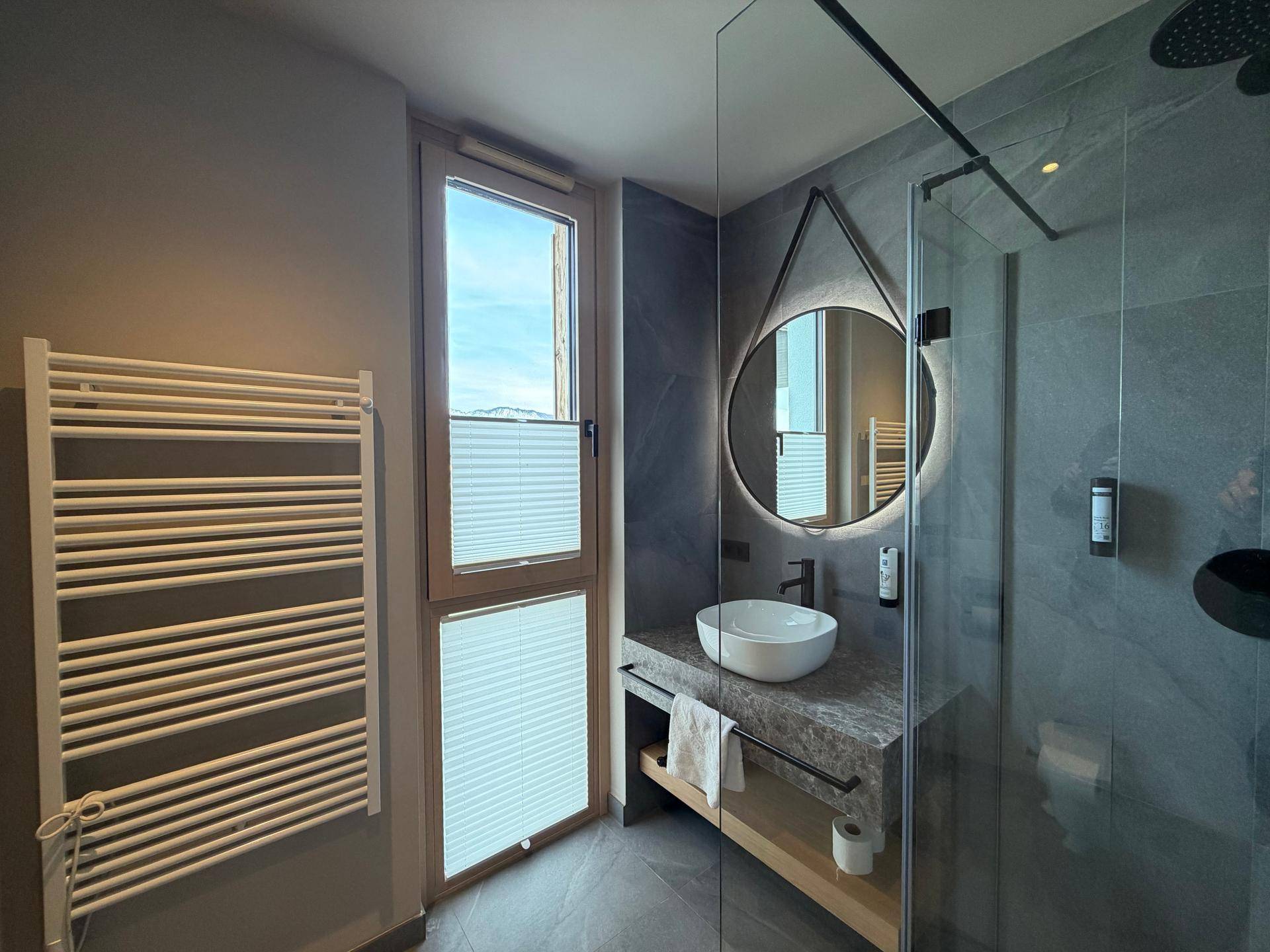 Helles Badezimmer mit Fenster, beheiztem Handtuchhalter und moderner Dusche.