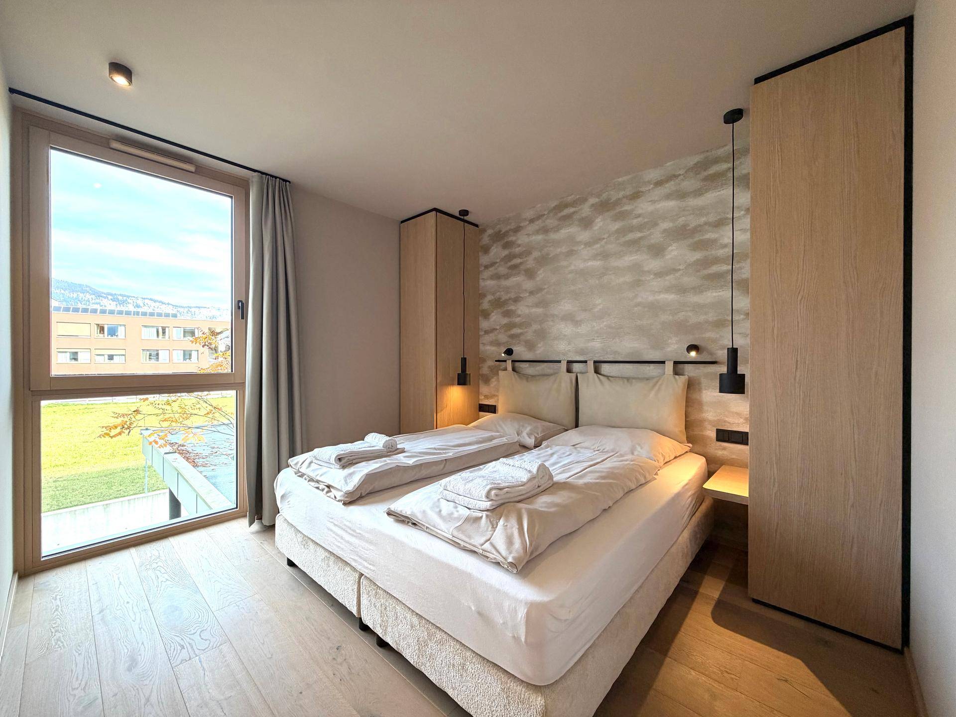 Modernes Schlafzimmer mit Doppelbett, Holzelementen und großem Fenster mit Bergblick.