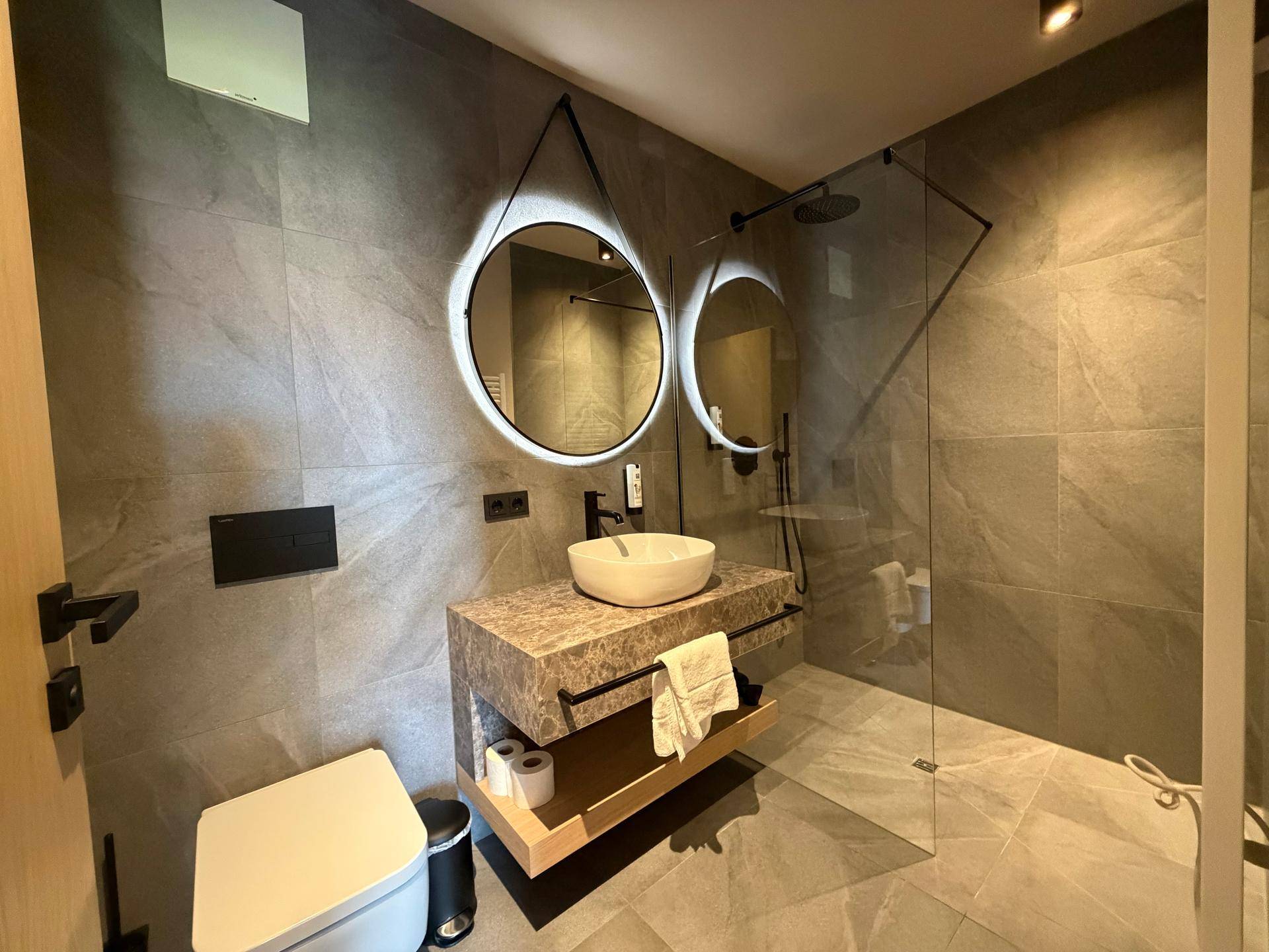 Elegantes Badezimmer mit grauen Fliesen, modernem Waschtisch und begehbarer Dusche.