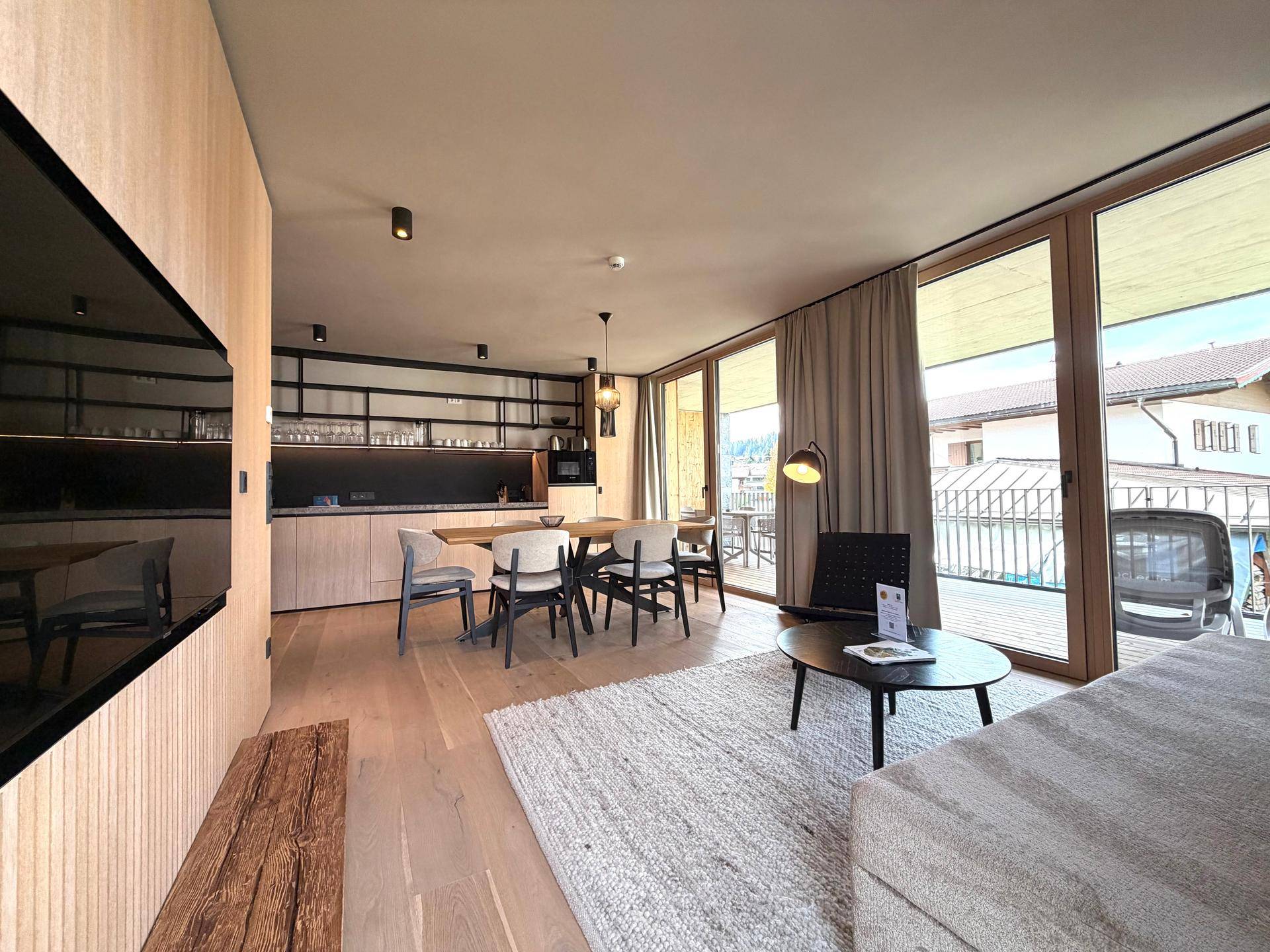 Offener Wohn-Essbereich mit moderner Küche, Holzboden und Zugang zum Balkon.