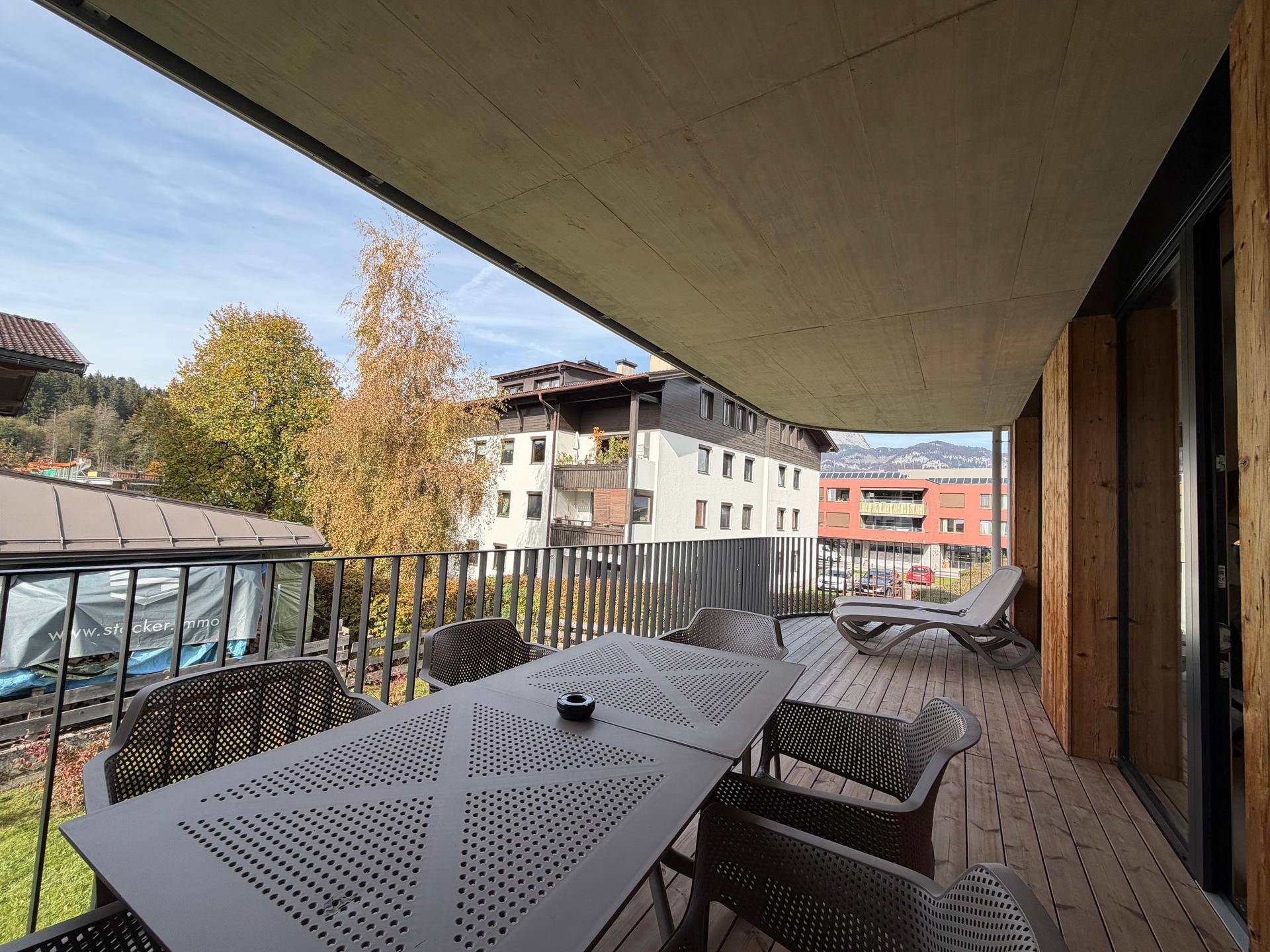 Geräumiger Balkon mit Holzboden, Esstisch und Liegestühlen, ideal zum Entspannen.