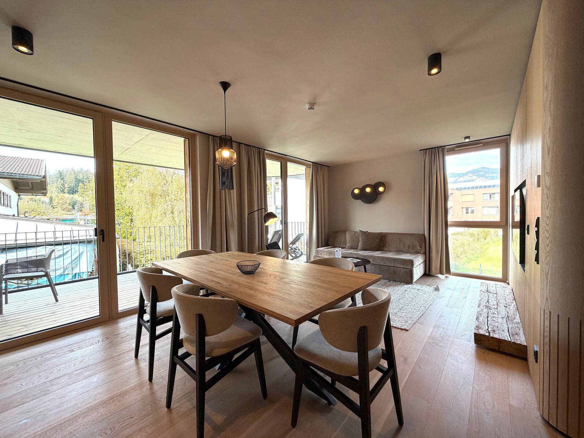 Geräumiger Wohn-Essbereich mit Holzboden, großen Fenstern und direktem Zugang zum Balkon.