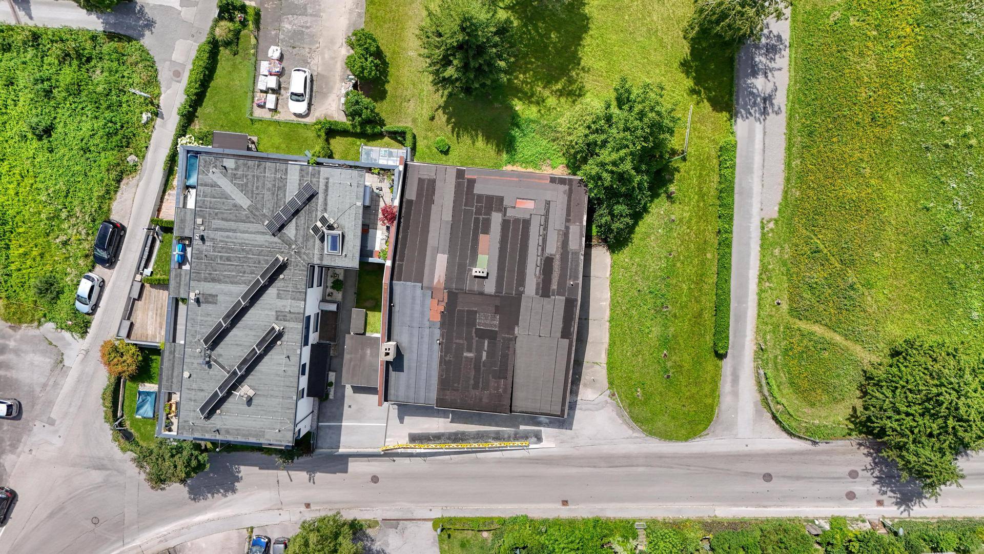 Draufsicht auf ein Gebäude mit Solaranlagen auf dem Dach, umgeben von grünen Rasenflächen und Wegen.